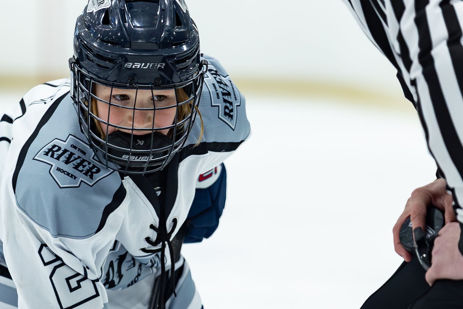 Young hockey player in River jersey looking up at referee during face-off.