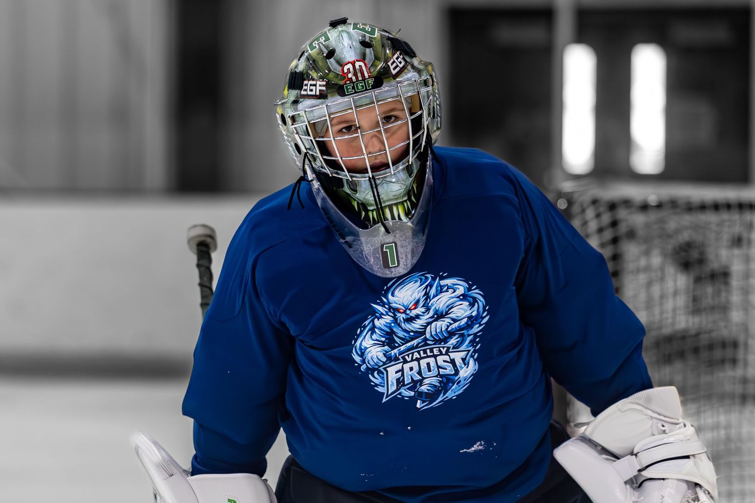 Youth hockey goalie in blue Frost jersey crouching in ready position on ice rink.