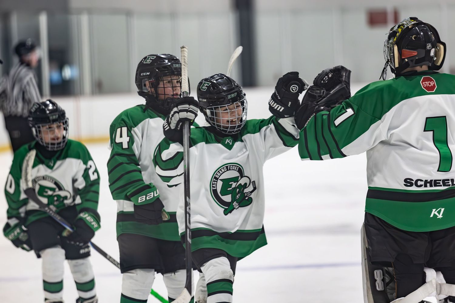Youth hockey players in green uniforms celebrating with high-fives near the goal.