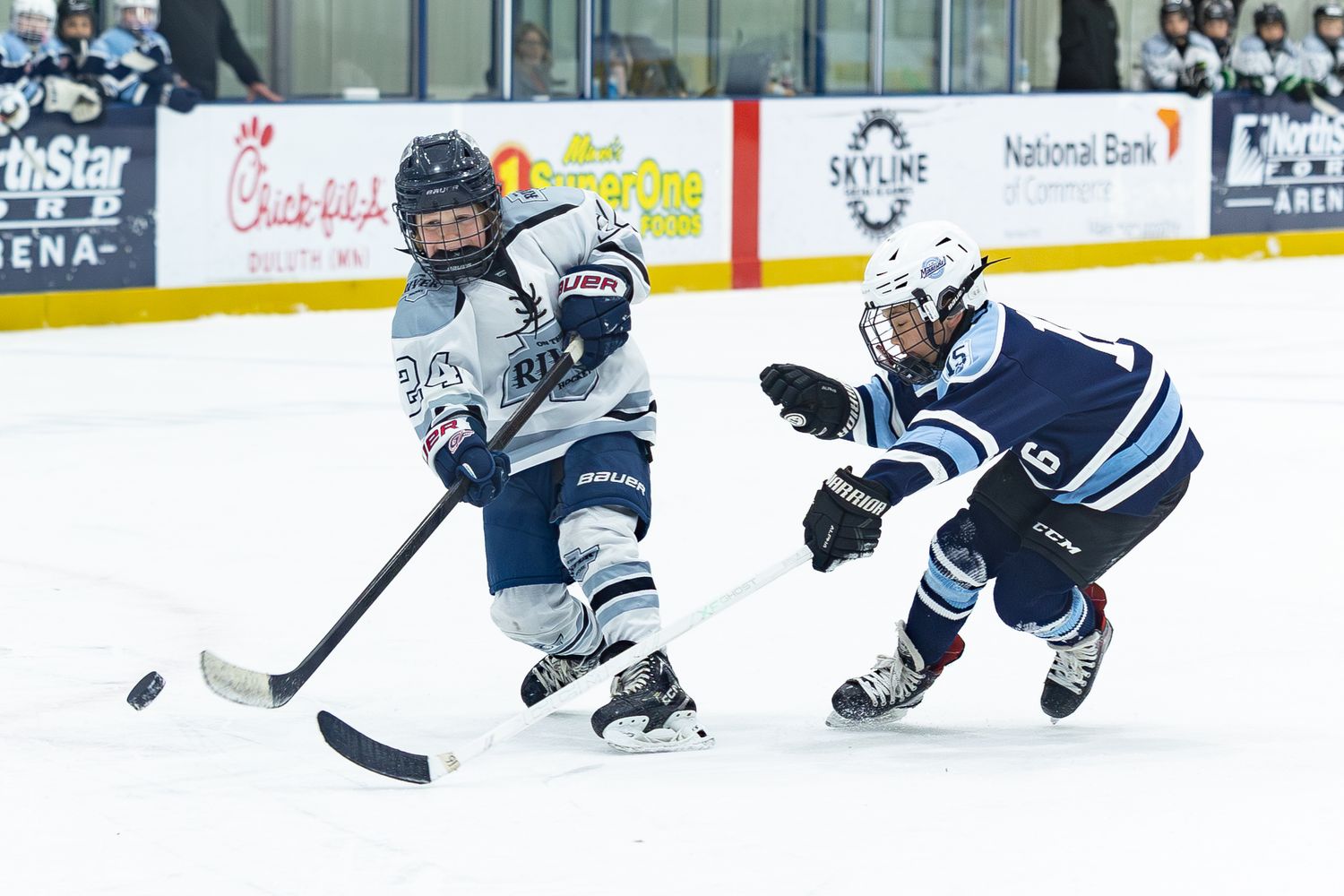 Youth hockey players compete on the ice as one player reaches for the puck during an intense game.