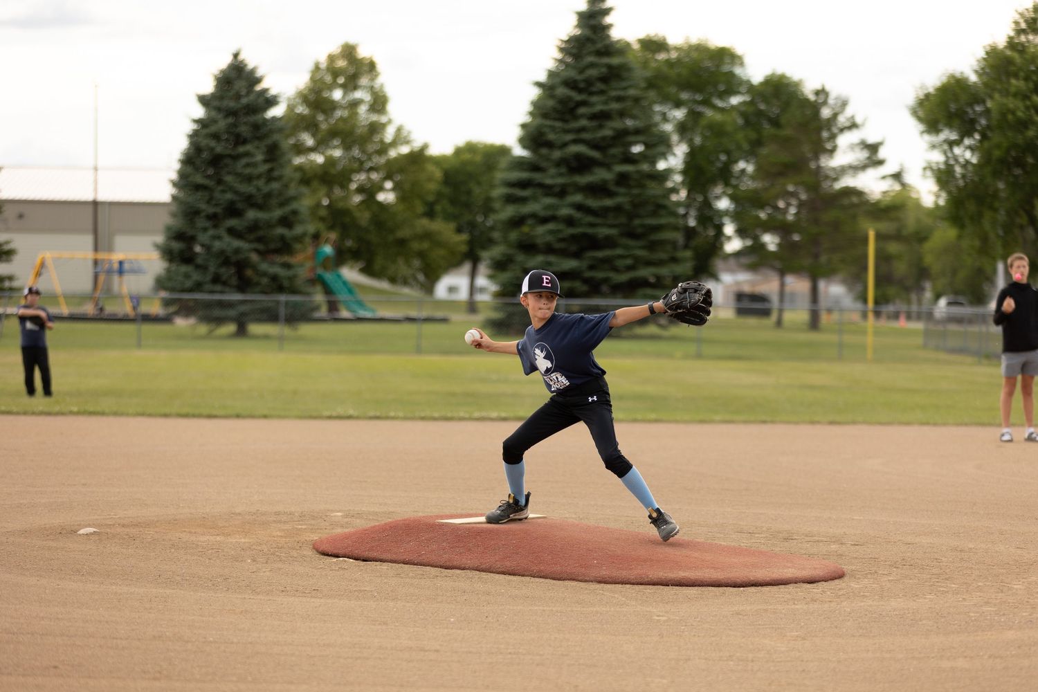 Youth baseball pitcher in navy uniform delivering pitch from mound during game.