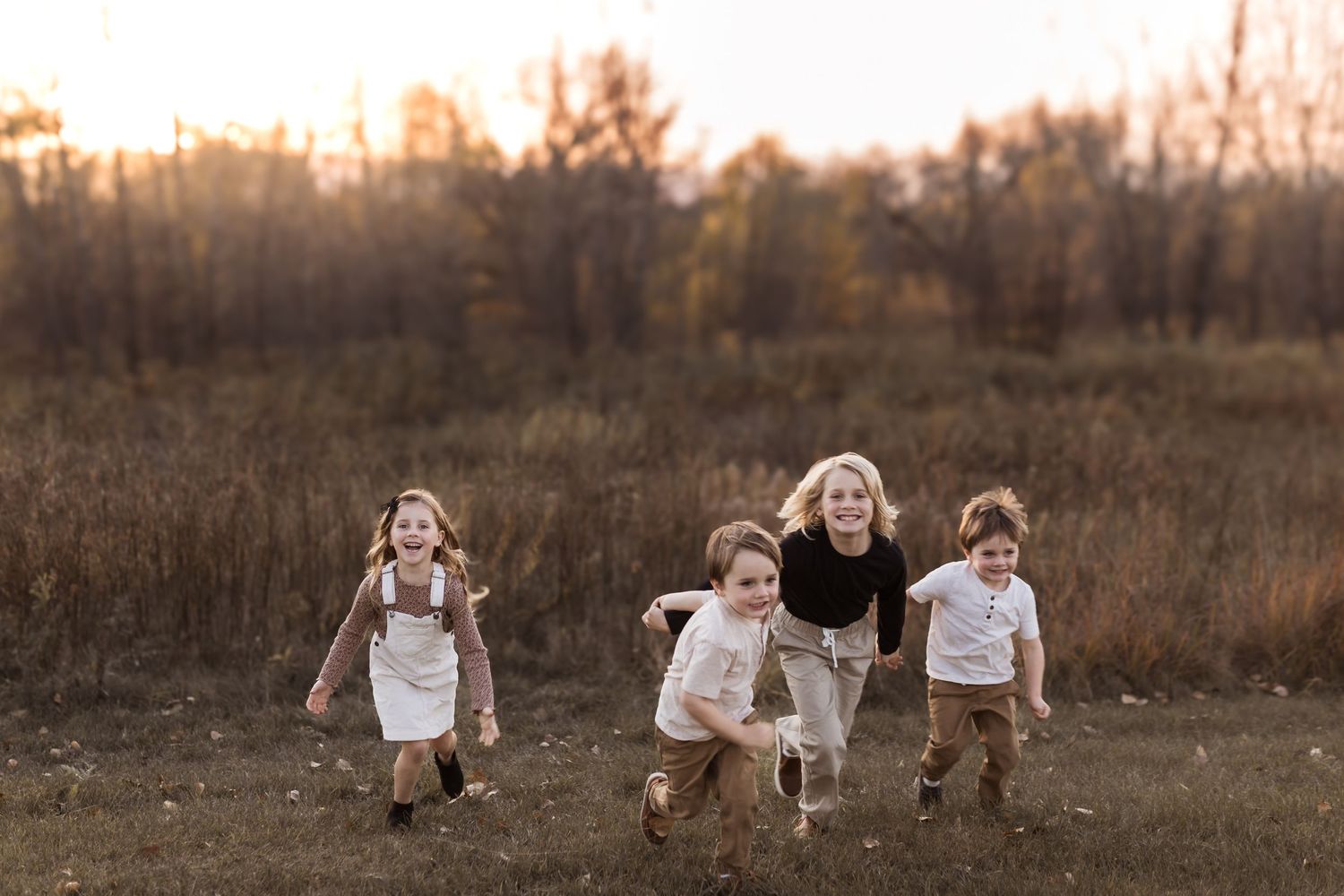 A woman and three young children run and laugh together through a golden field at sunset in autumn.