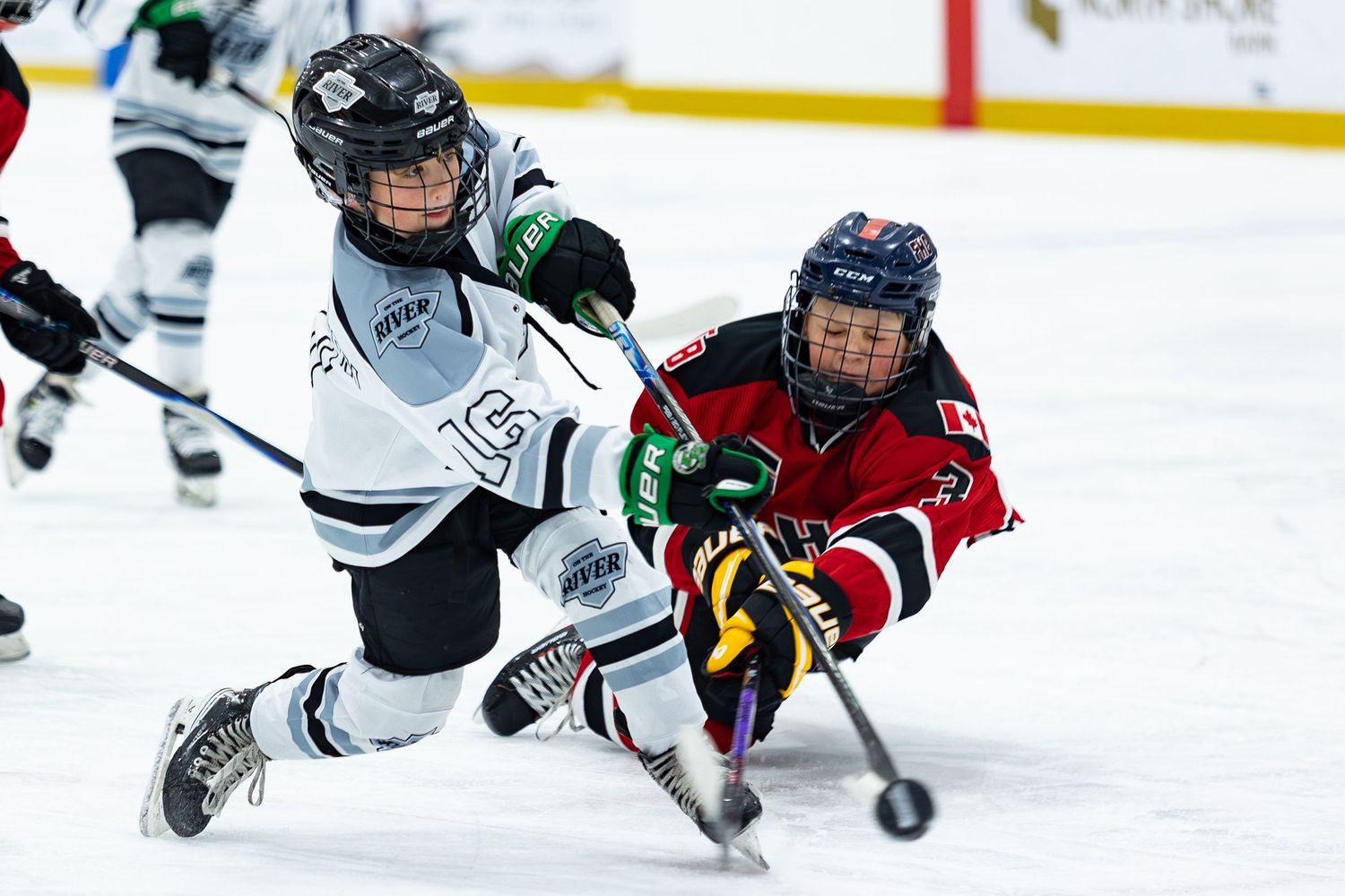 Two youth hockey players collide during intense game, one falling on ice.
