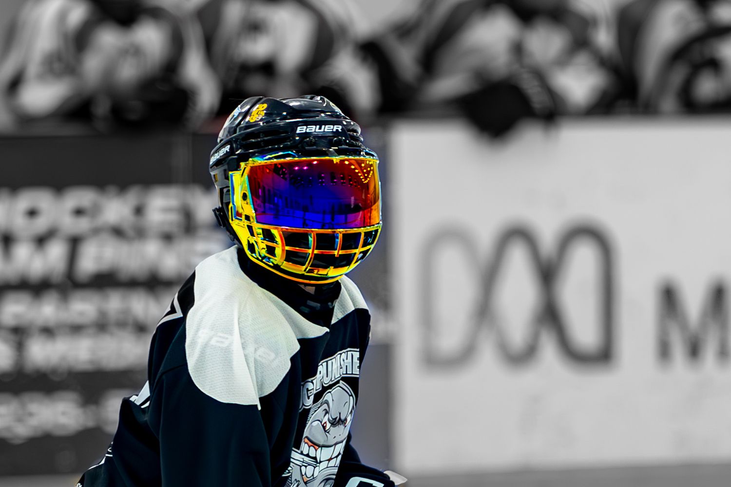Young hockey player wearing colorful rainbow visor helmet in black and white action photo.