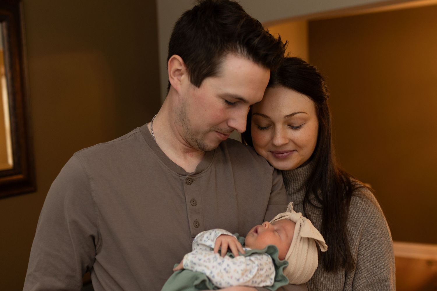 New parents gently cradle their newborn baby in a hospital room, sharing a tender family moment.