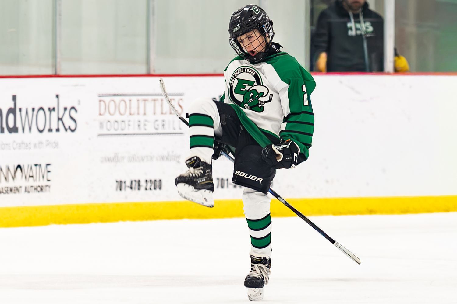Young hockey player in green uniform skating and shooting on ice during a youth hockey game.