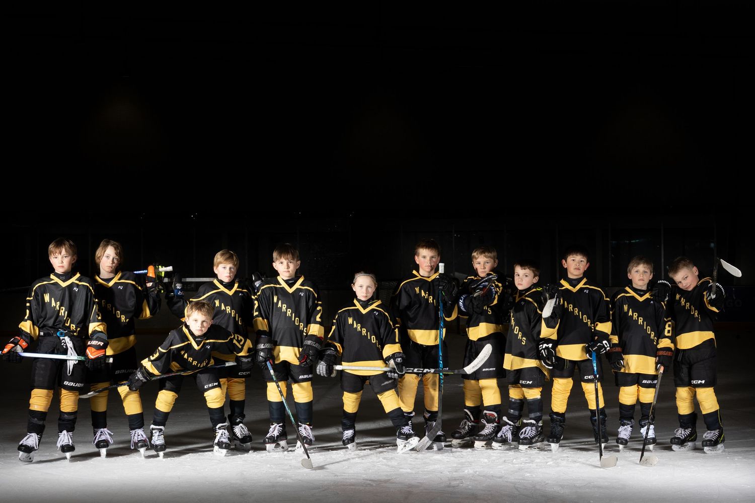 Youth hockey team in black and gold uniforms posing together on dark ice rink.