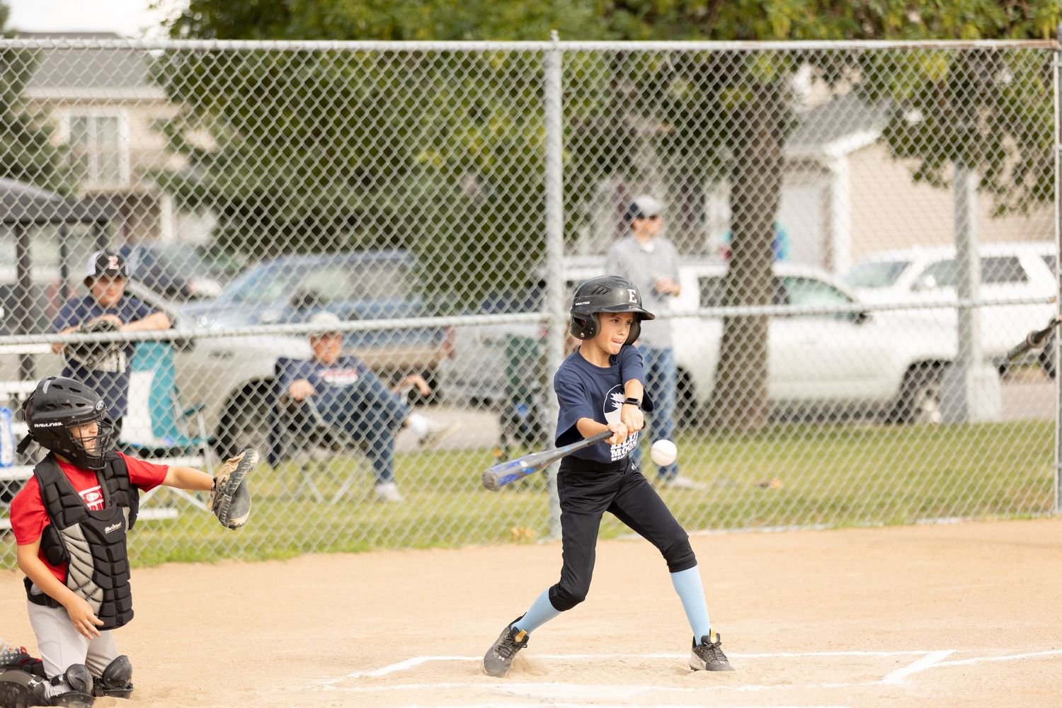 Young baseball player in navy uniform batting at home plate during youth game.