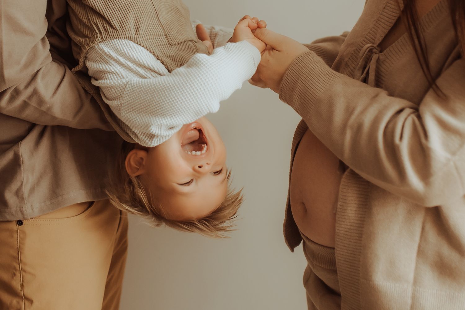 Playful parents holding their laughing toddler upside down in a bright indoor setting.