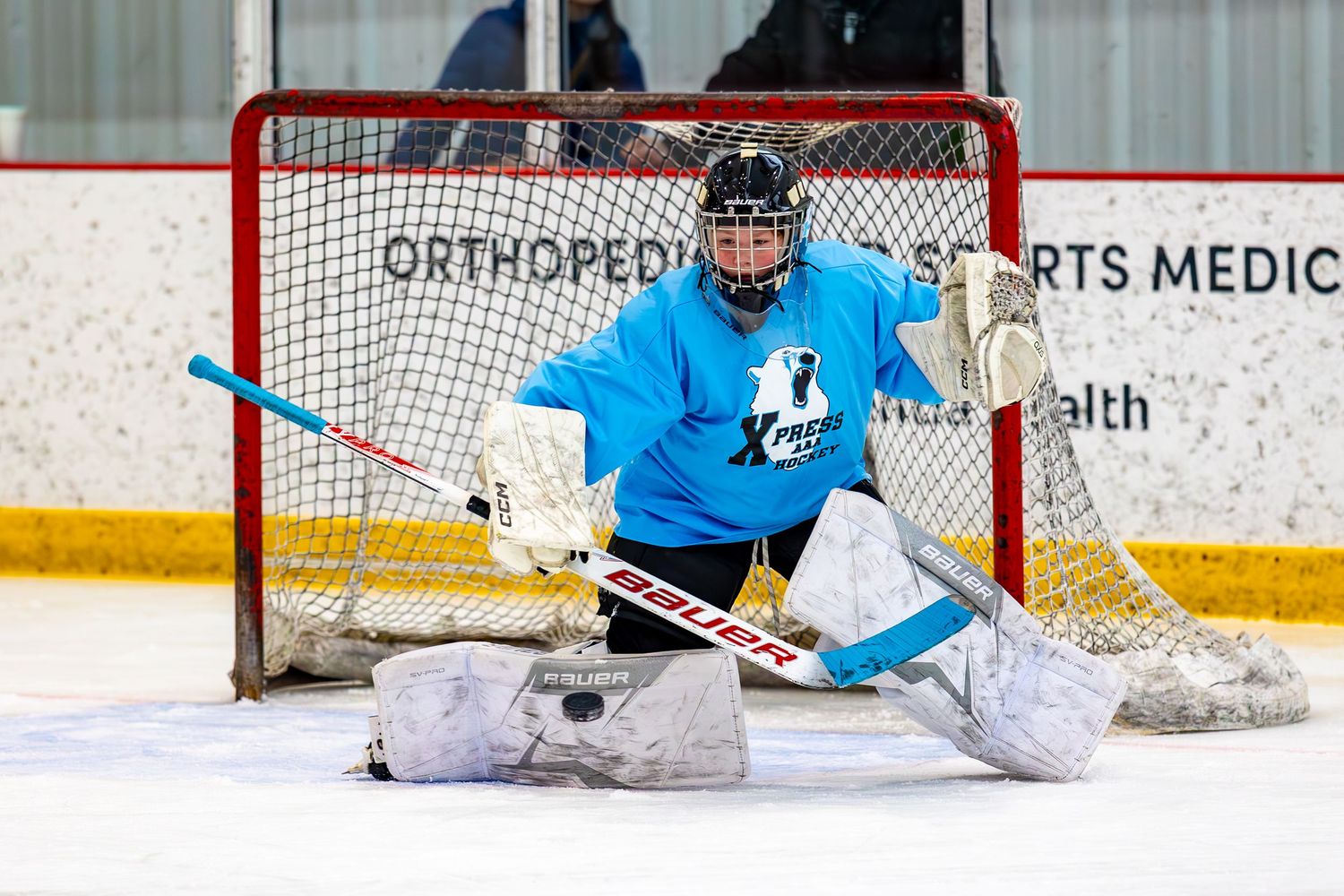 Youth hockey goalie in blue jersey in butterfly position guarding net during practice.