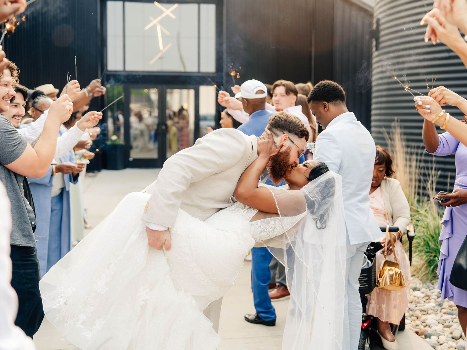 Romantic wedding exit with guests cheering as couple shares celebratory kiss.