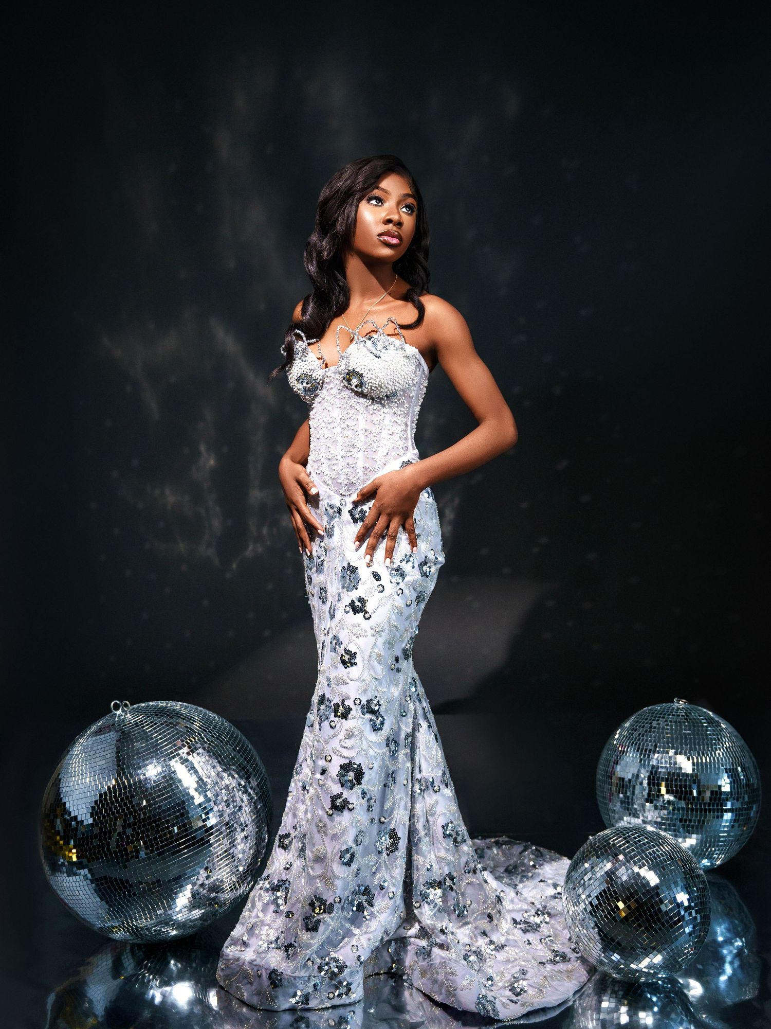 Elegant floral mermaid gown posed with disco balls against dark background in glamorous fashion photoshoot.