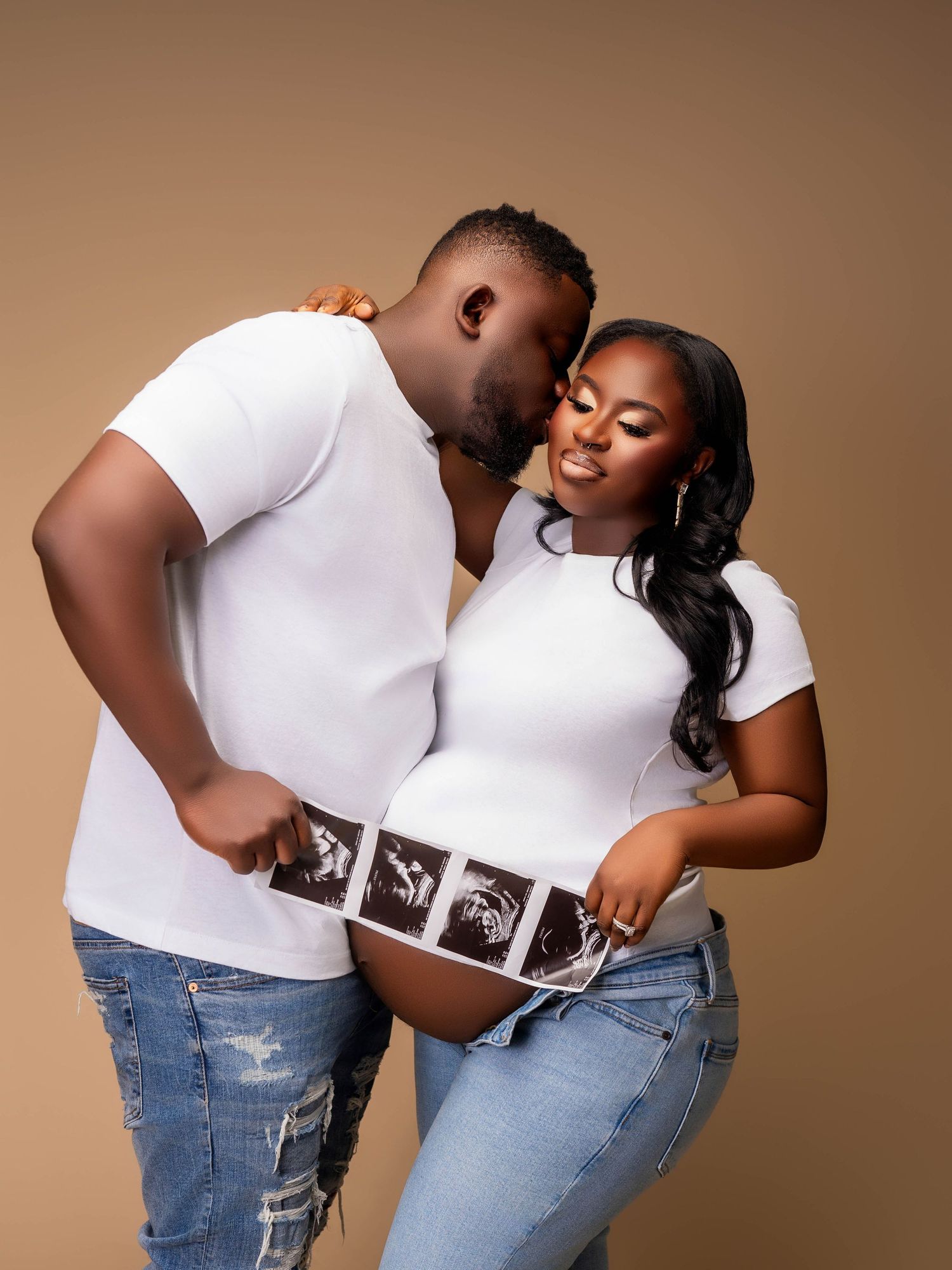 Expecting couple in white sharing intimate moment while displaying ultrasound photos.