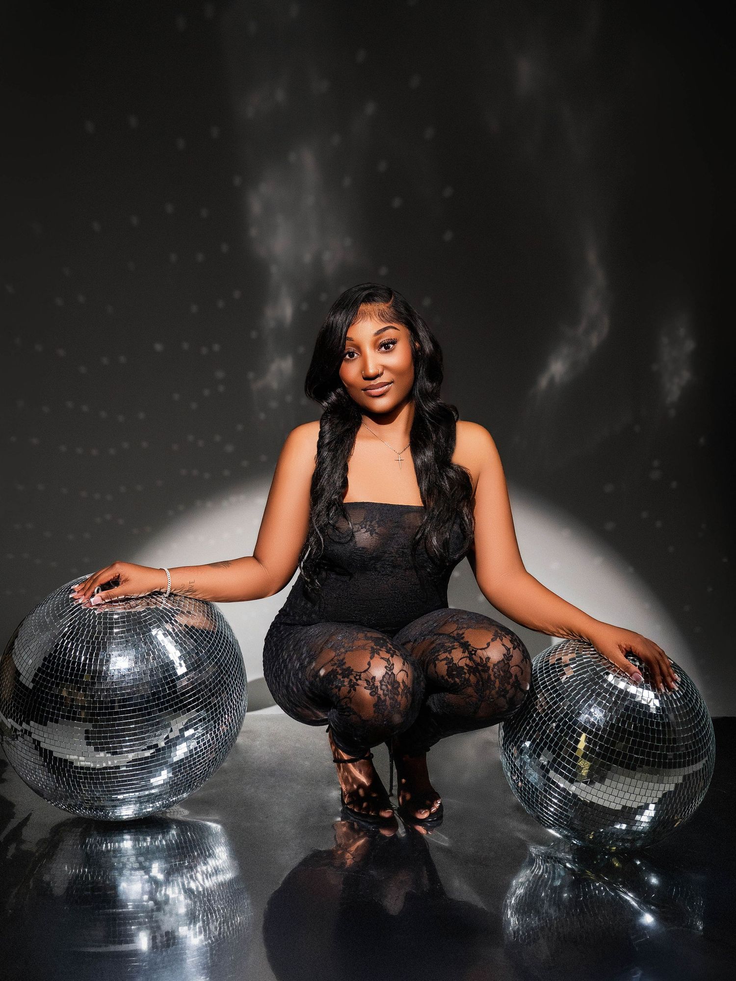 Stylish person in black dress posing with disco balls on dark reflective surface.
