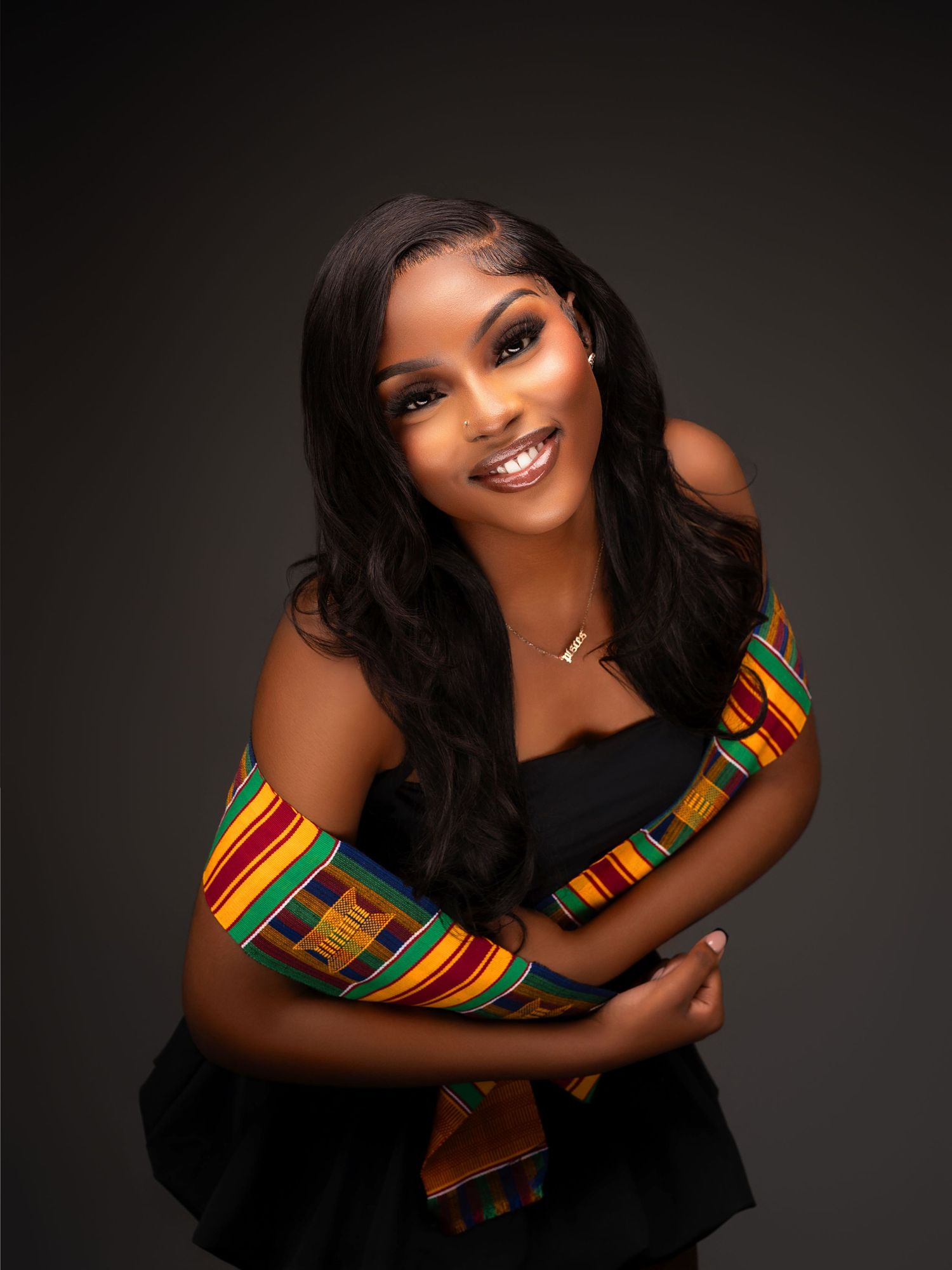 Studio portrait featuring traditional African kente cloth accent against dark background.
