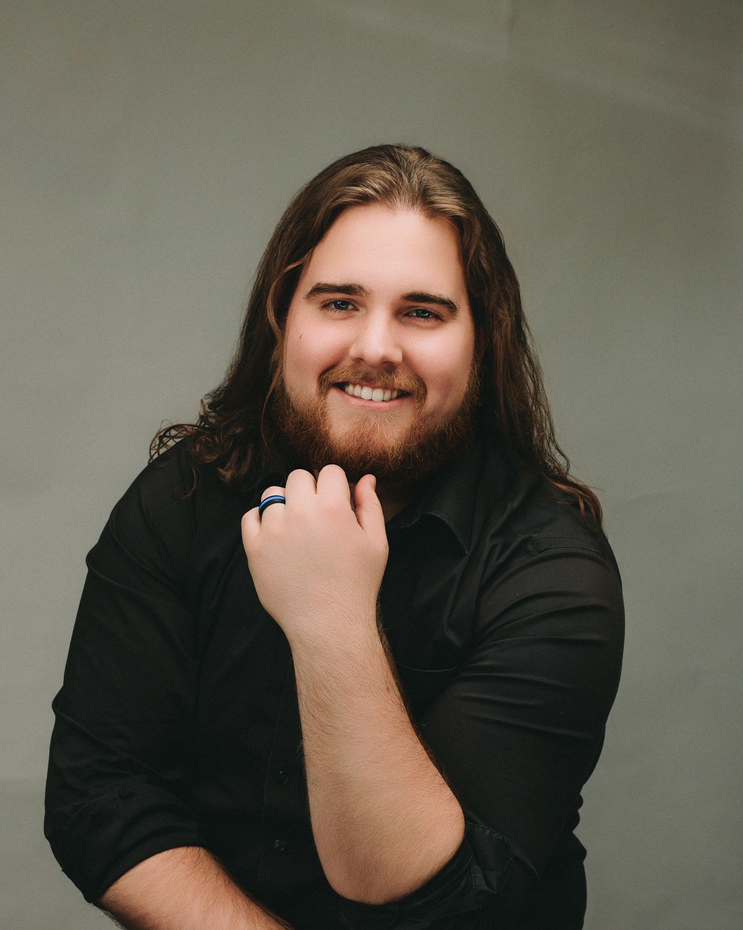 Studio portrait of person in black attire smiling warmly against light gray backdrop.