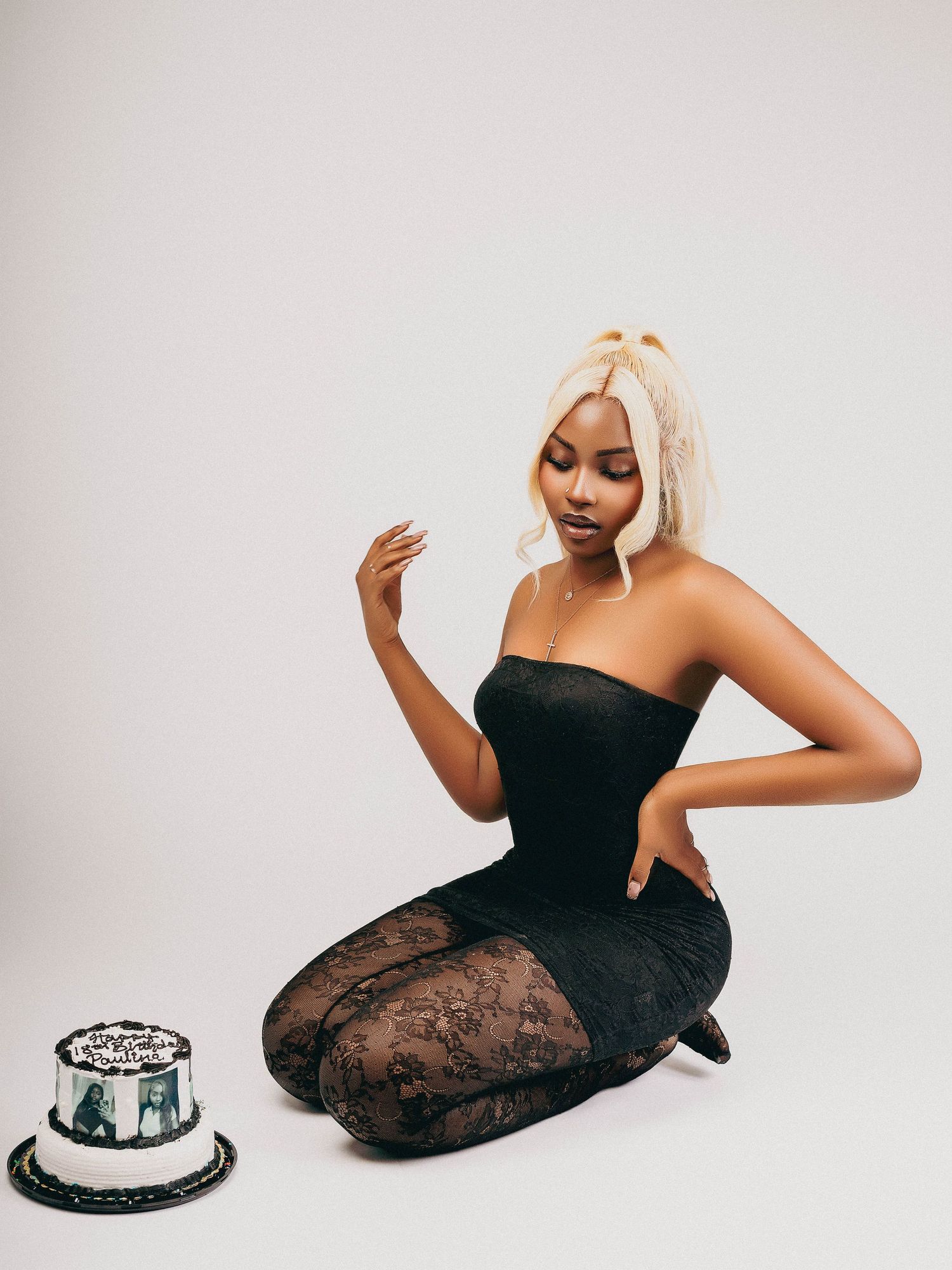 Elegant portrait with black lace dress and a decorative cake on white background.