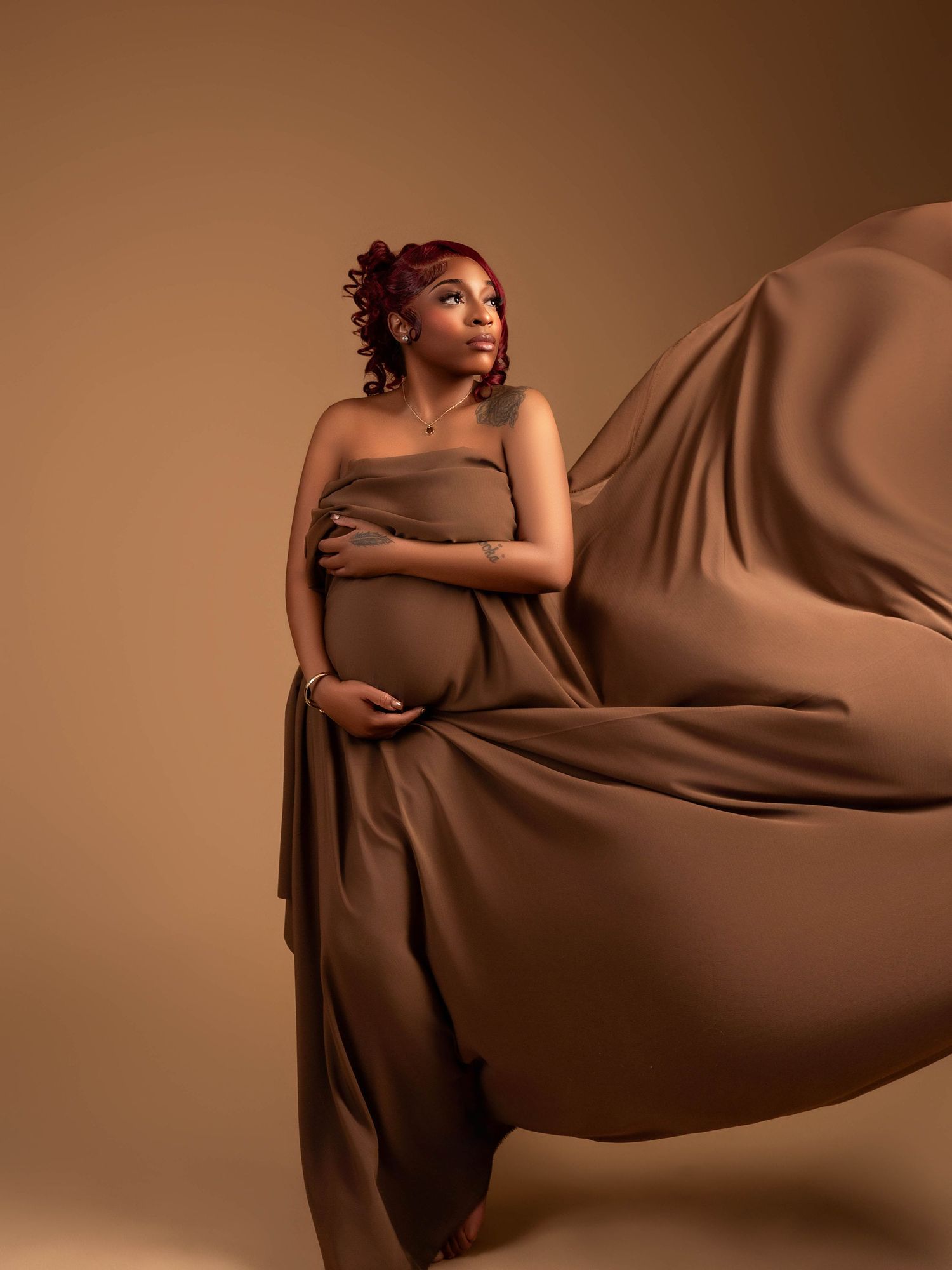 Maternity photo featuring flowing brown fabric against warm brown background.