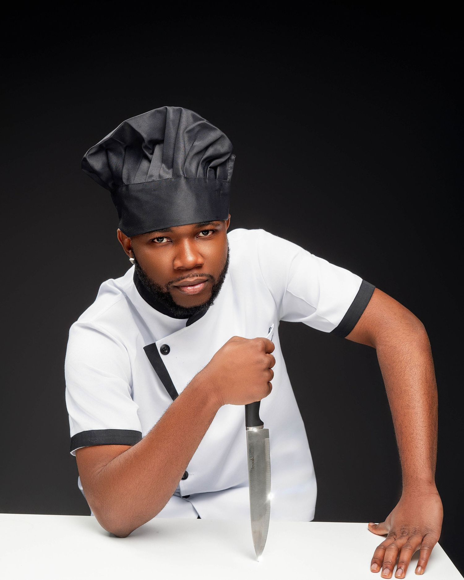 Man in white polo shirt posing creatively on white surface against black backdrop.
