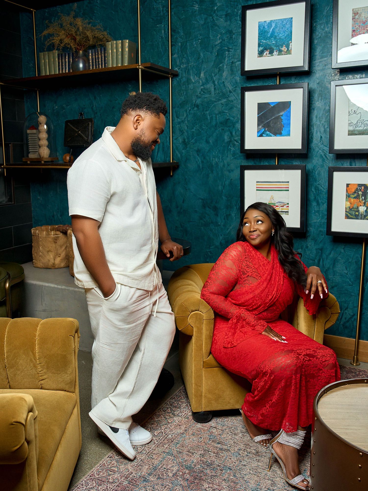 Two people sharing a conversation in an elegant teal room with vintage furniture and framed artwork.