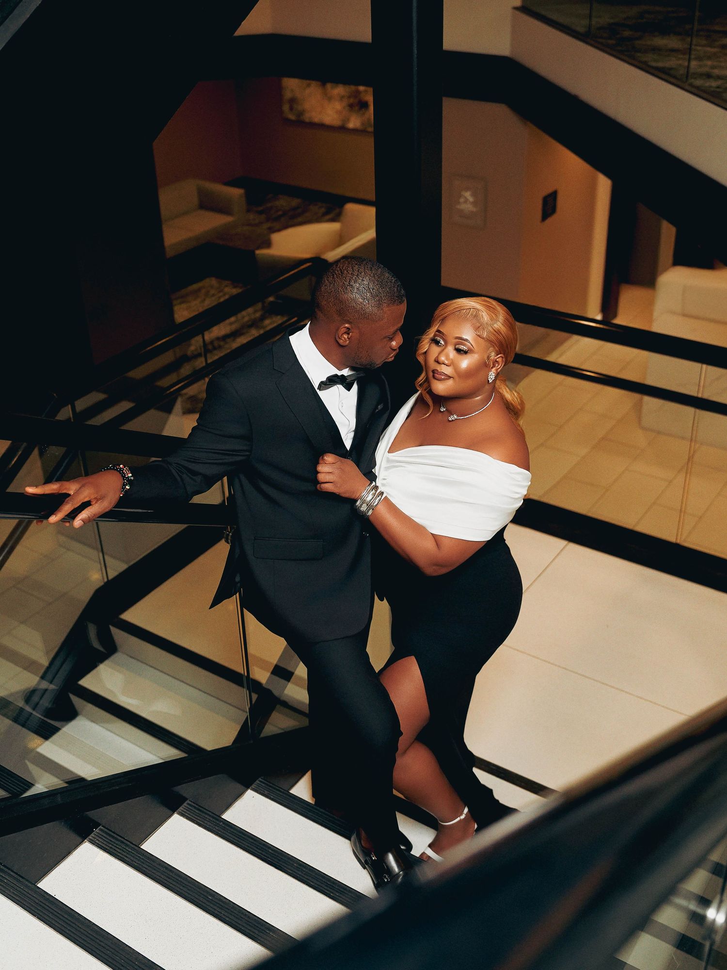 A stylish couple shares an intimate moment on modern black and white stairs.