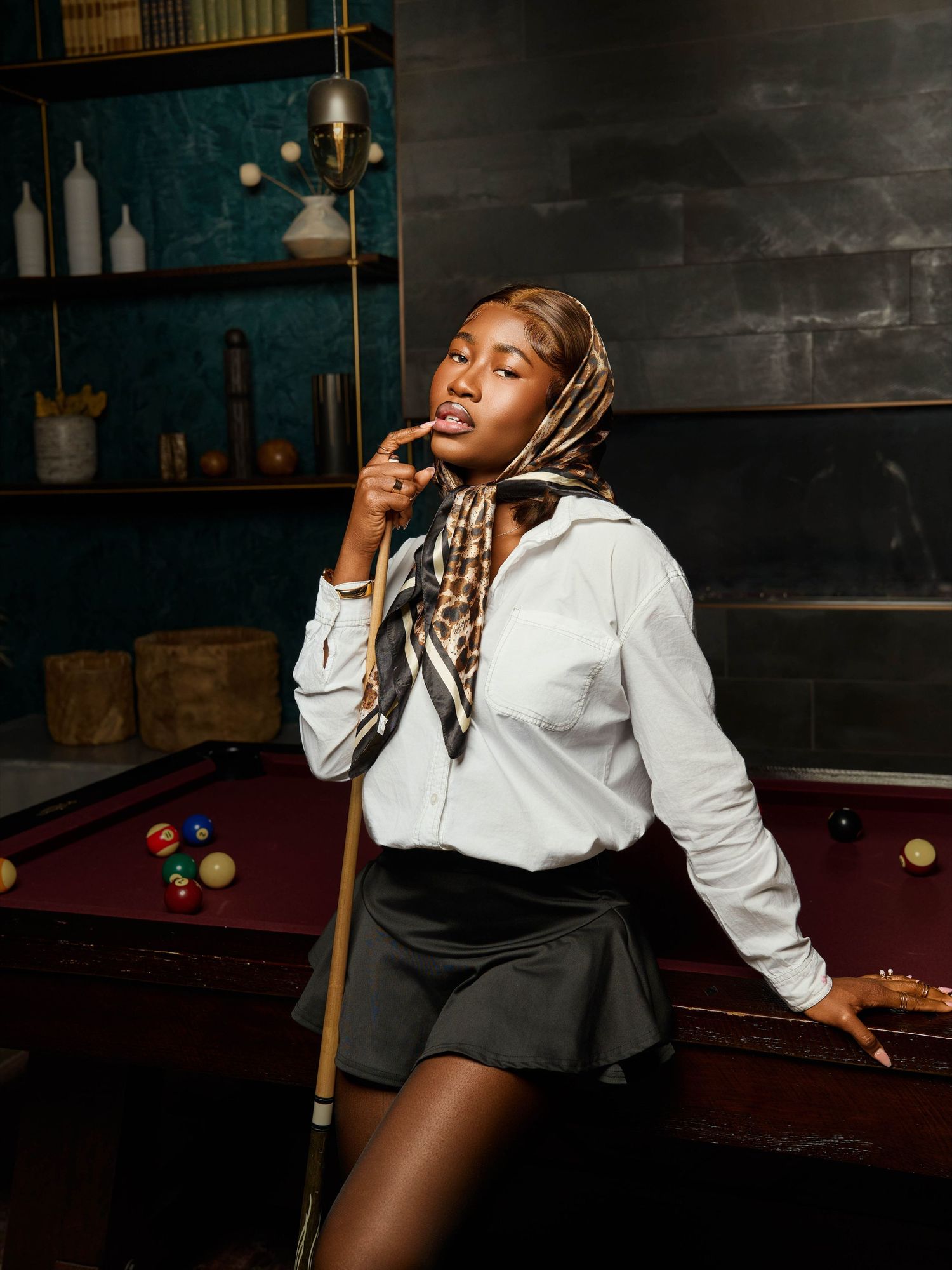 Fashion portrait in a pool hall featuring a model in preppy attire leaning against a billiards table.
