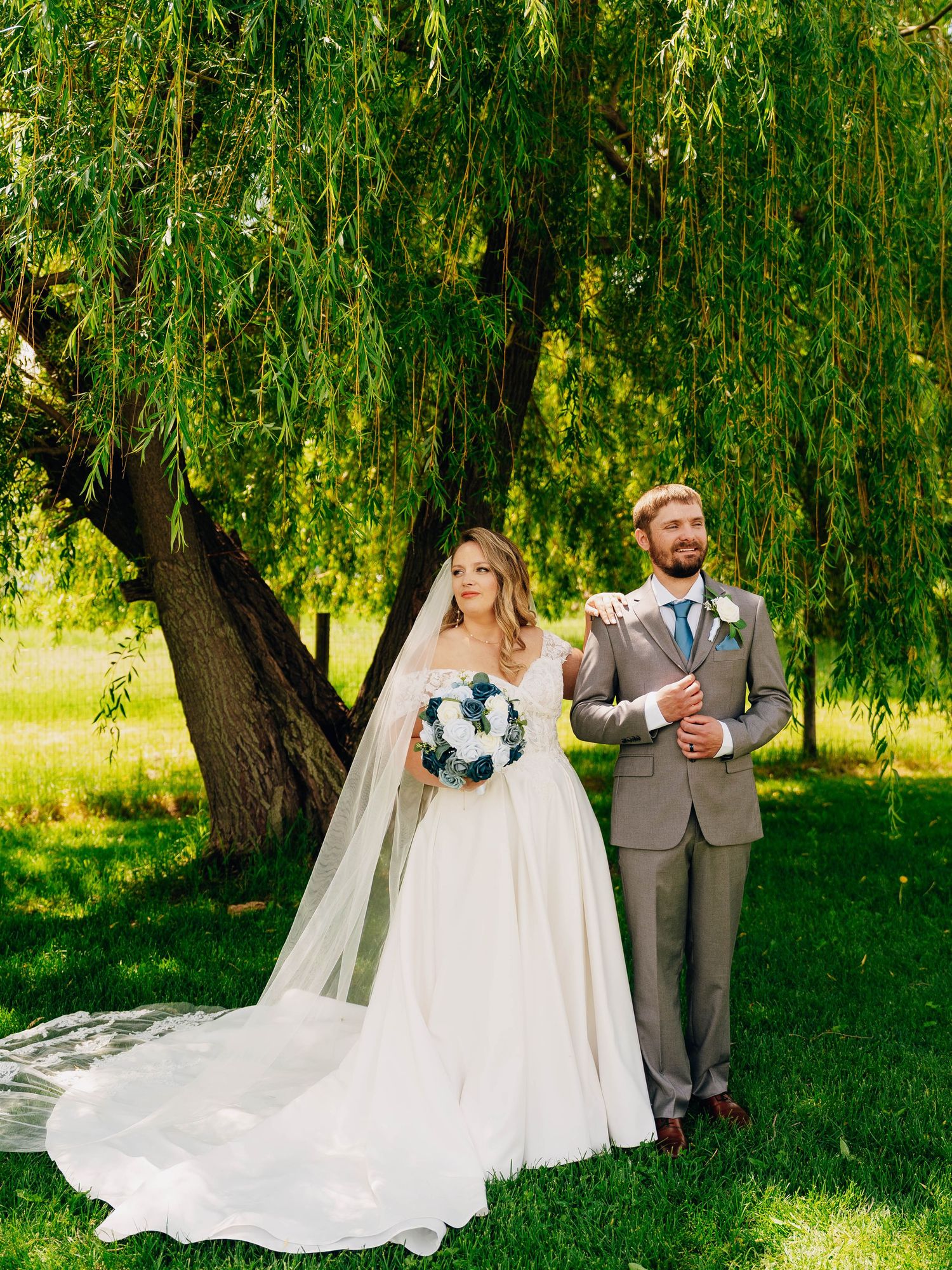 Bride and groom standing together under a weeping willow tree during outdoor wedding ceremony.