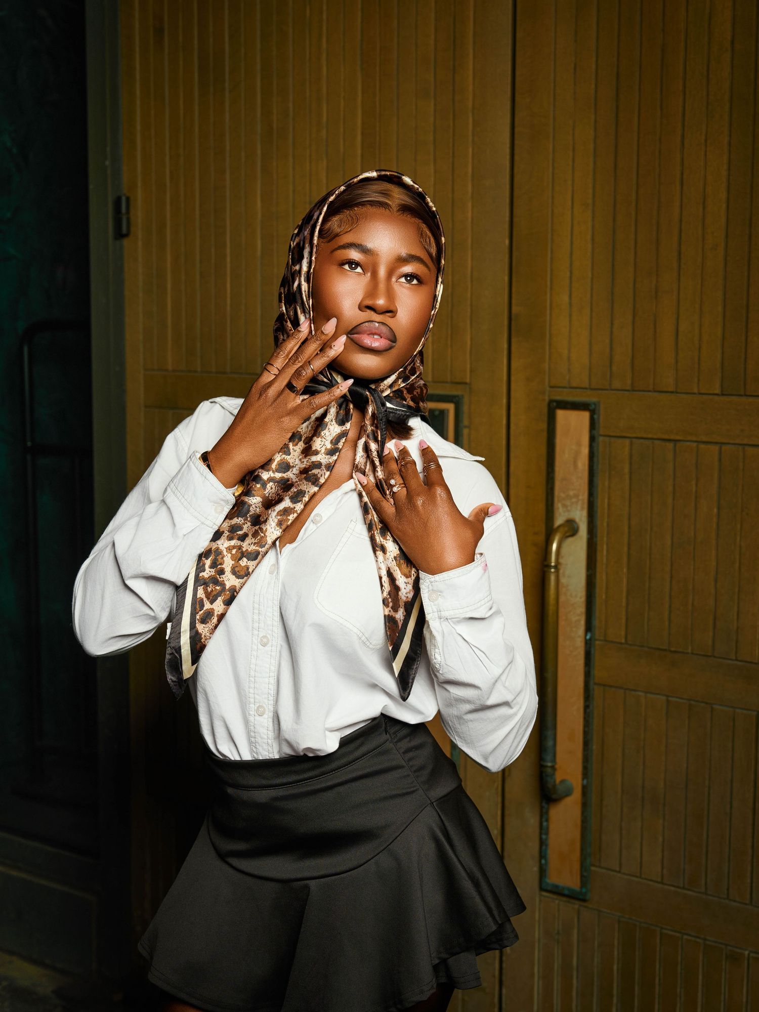 Stylish portrait featuring a model in a white blouse and leopard print headscarf against a wooden door.