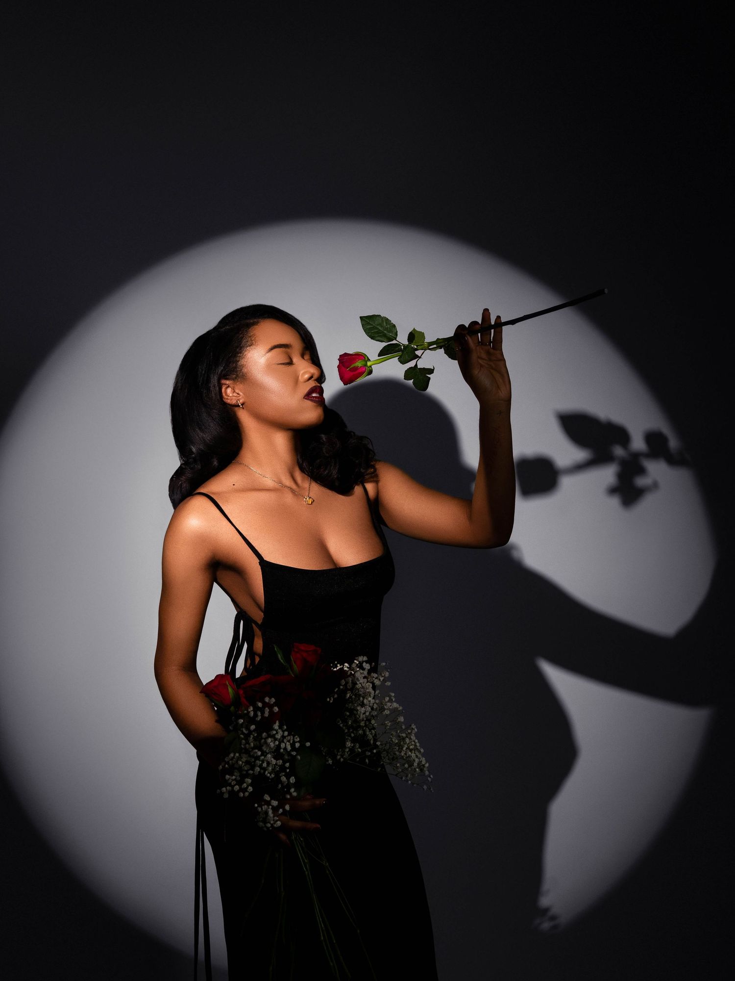 Artistic portrait with a single rose against dramatic spotlight creating shadow effects.