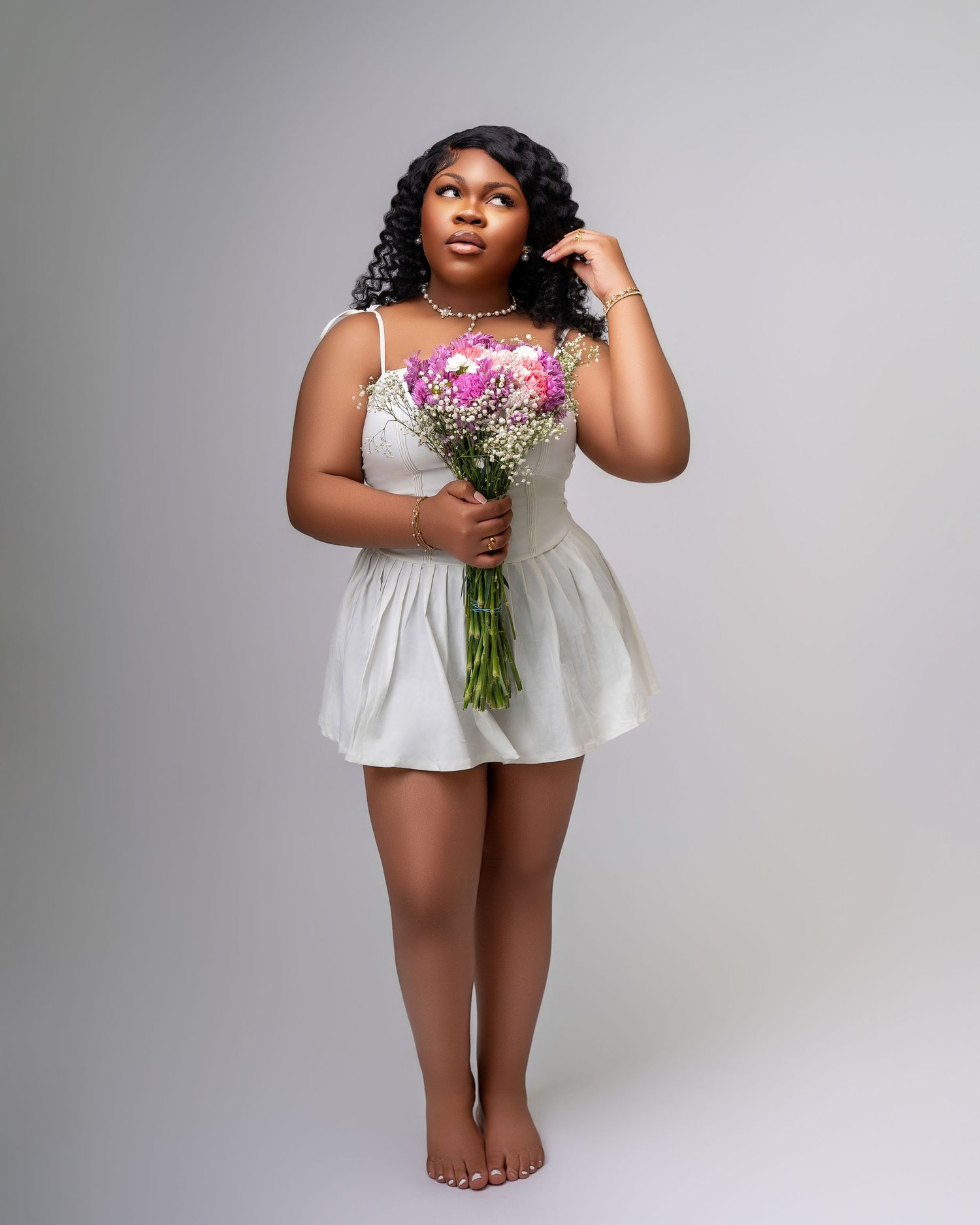 Romantic portrait of woman in white sundress holding pink flower bouquet.