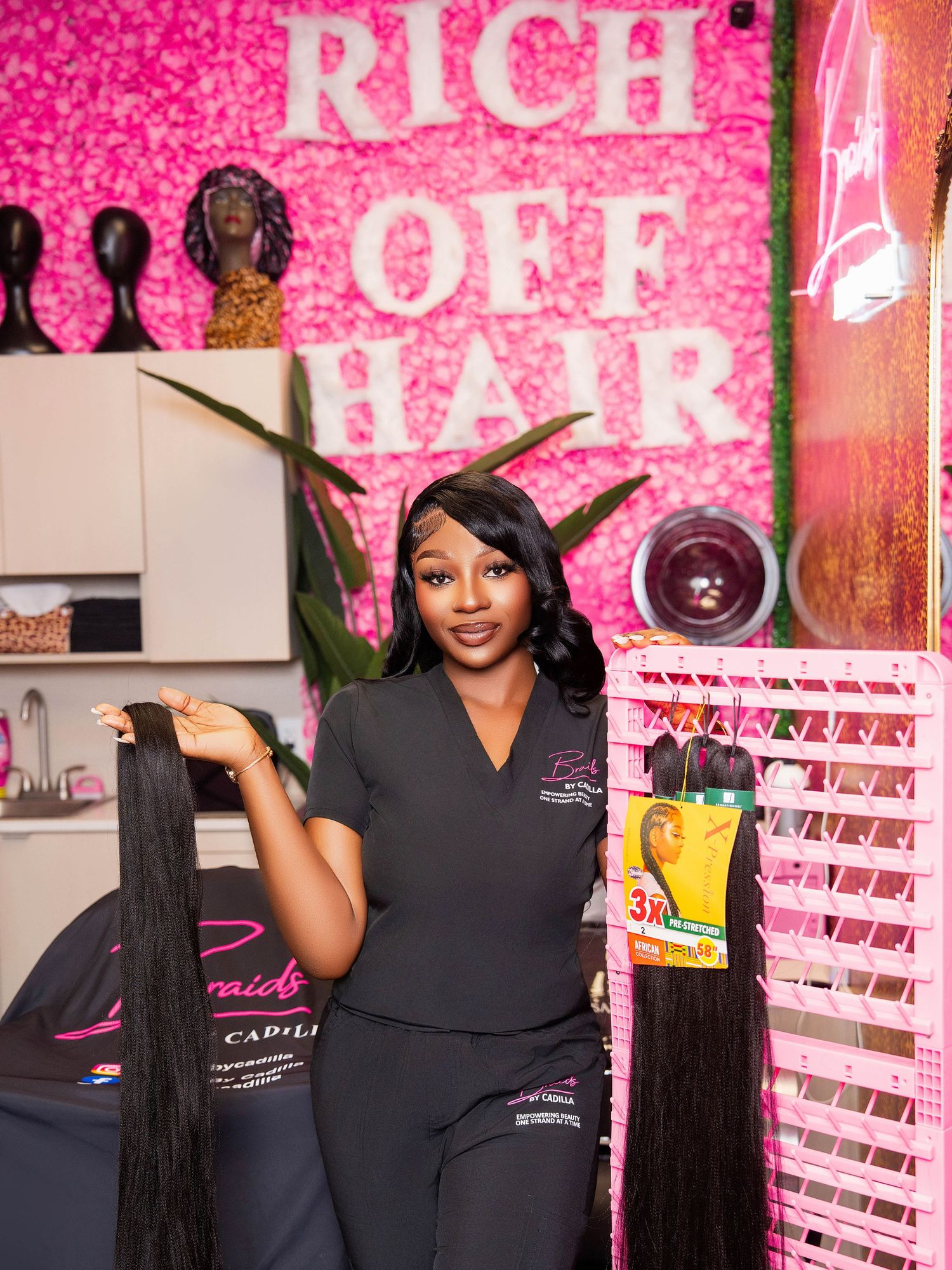Professional hairstylist demonstrating services in salon with pink glitter wall backdrop.