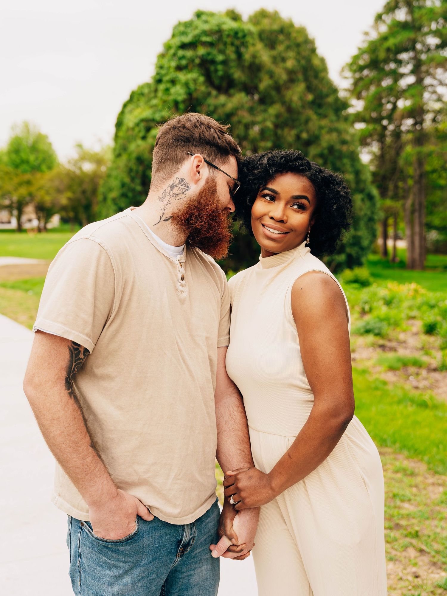 Intimate couple portrait in park setting surrounded by lush green foliage.