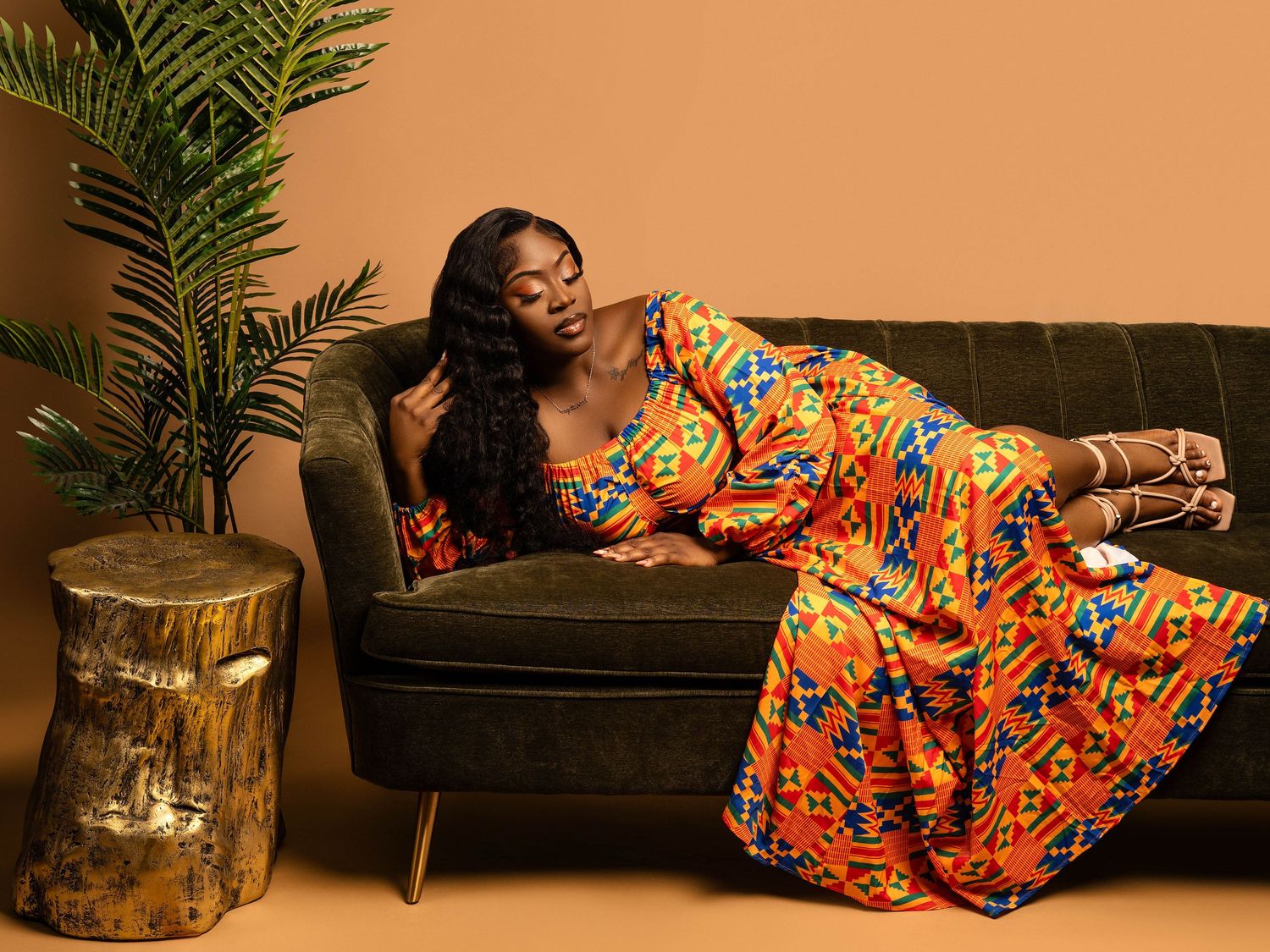 Fashion shoot featuring model in traditional African print dress posing on vintage couch.
