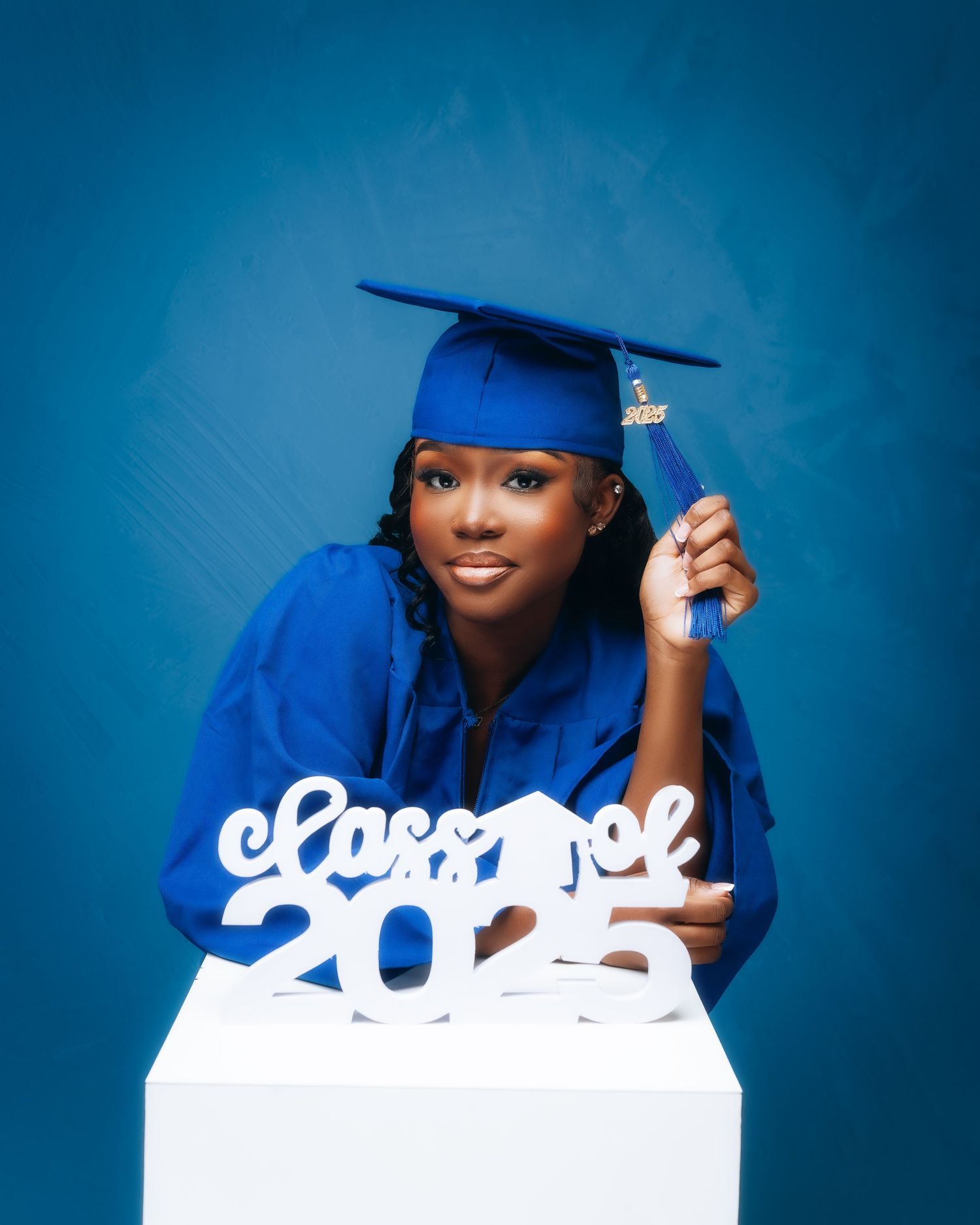 Graduate posing in blue cap and gown against vibrant blue backdrop with white text overlay.