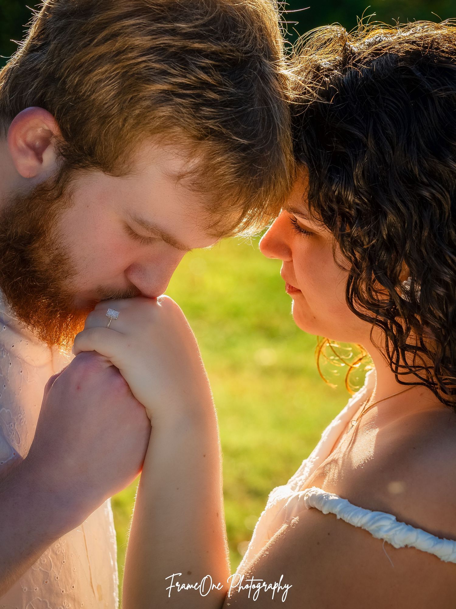 A tender romantic moment captured in warm sunlight between a couple sharing an intimate gesture outdoors.