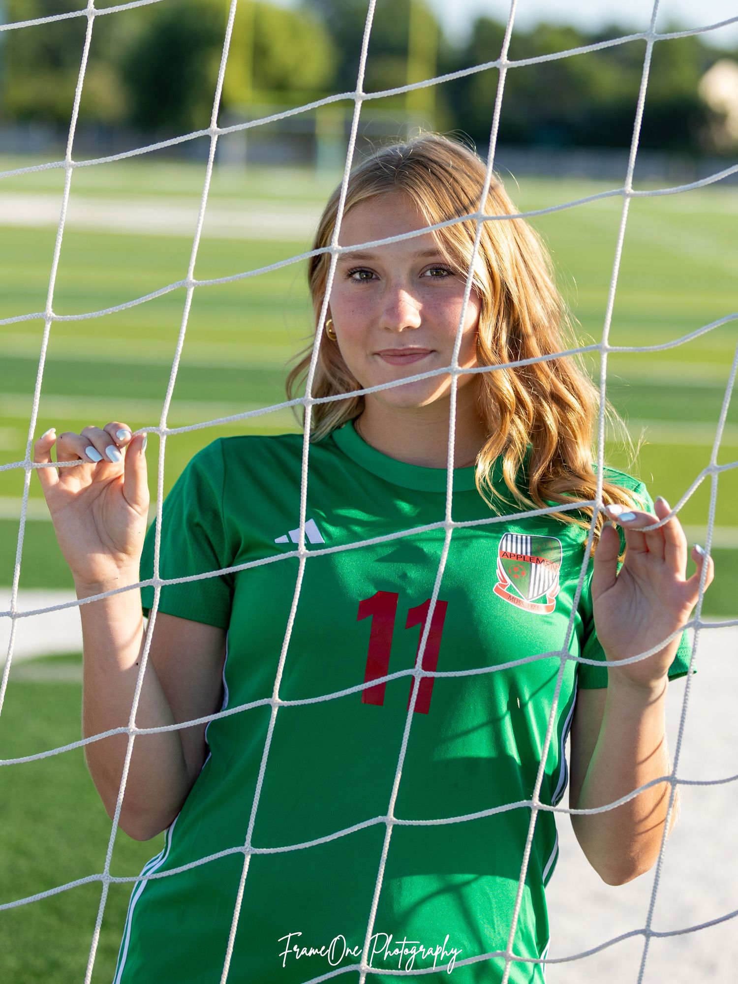 Soccer player in green jersey #11 poses next to goal net during golden hour on sunny sports field.