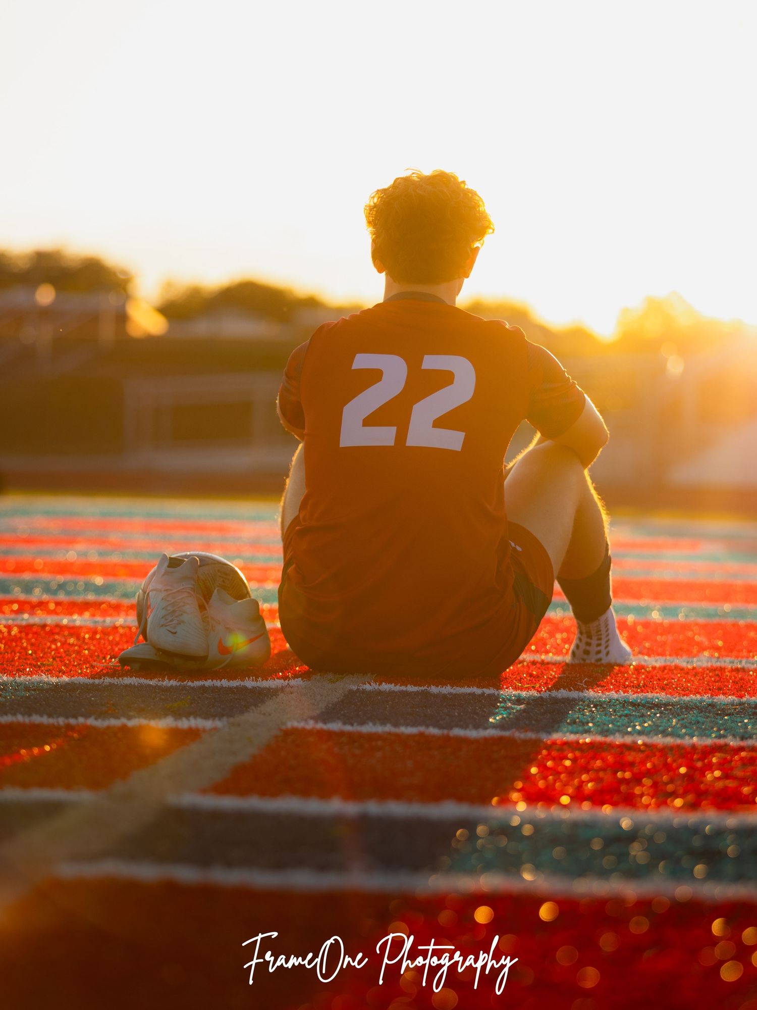 Silhouette of athletes sitting on field during golden sunset with jersey number 22 visible against warm glowing background.