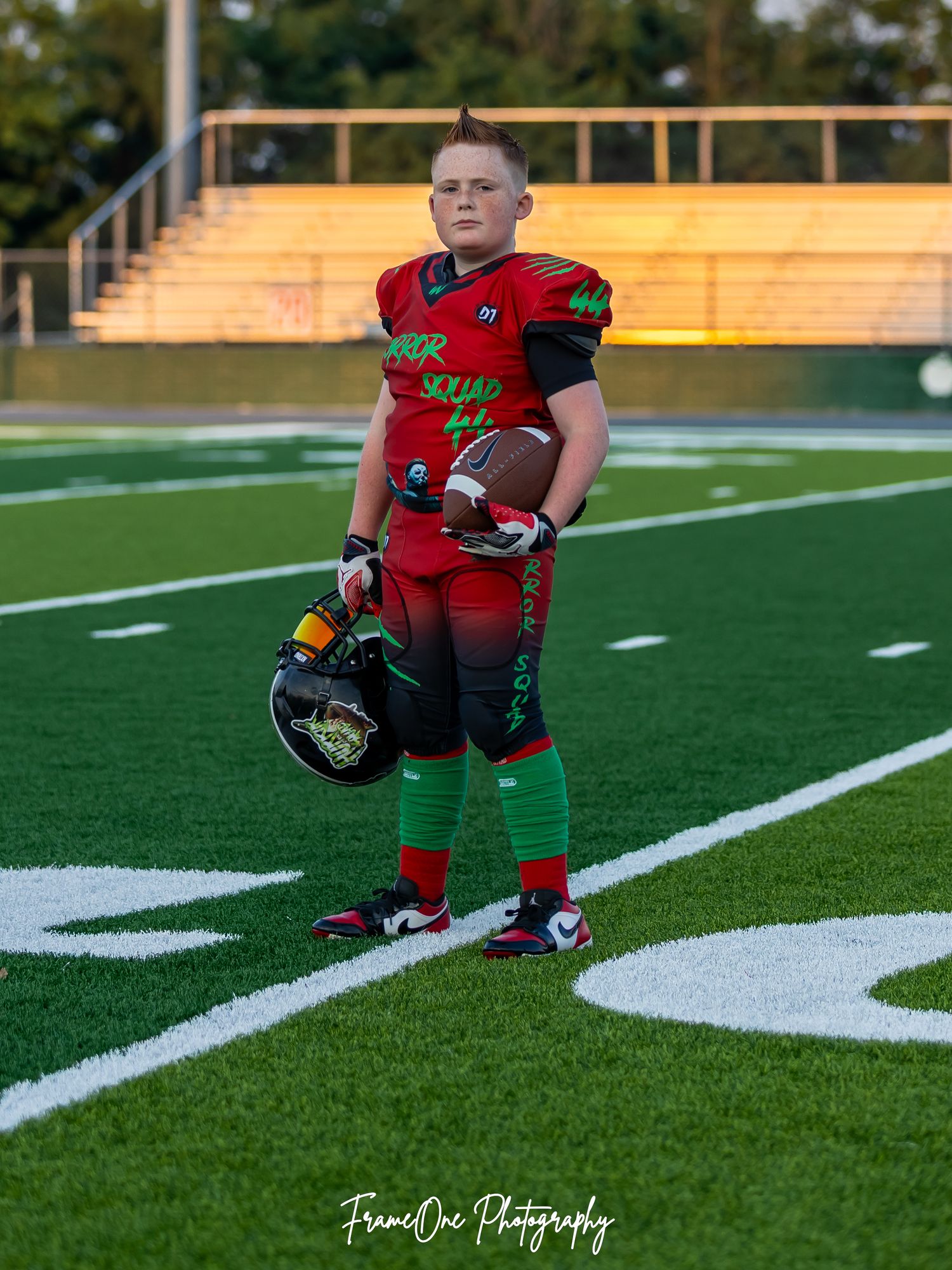 Young football player kneeling on turf field during practice or photo session showing game-ready stance and confidence.