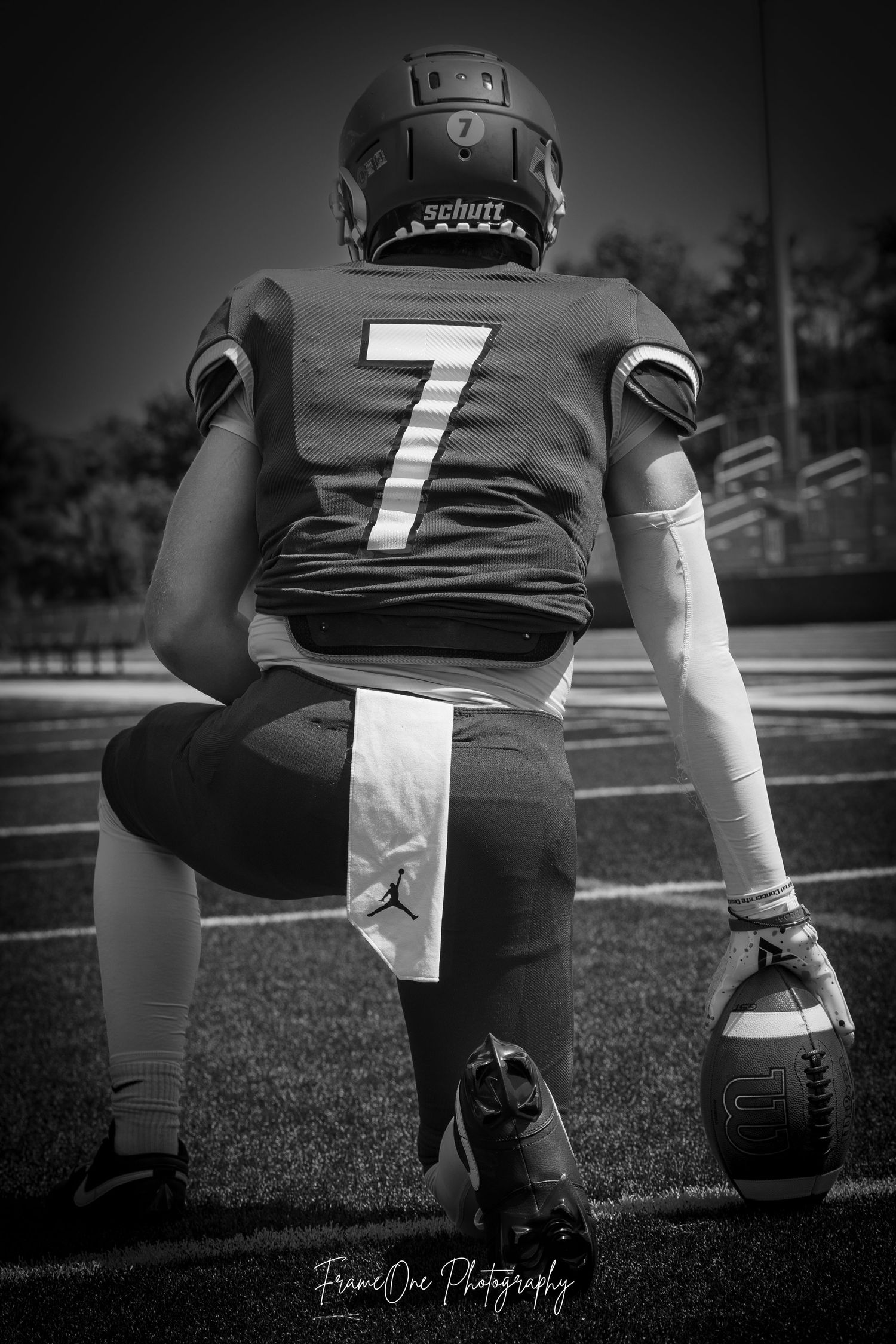 Black and white sports photo showing a football player wearing jersey number 7 kneeling on the field with a football.