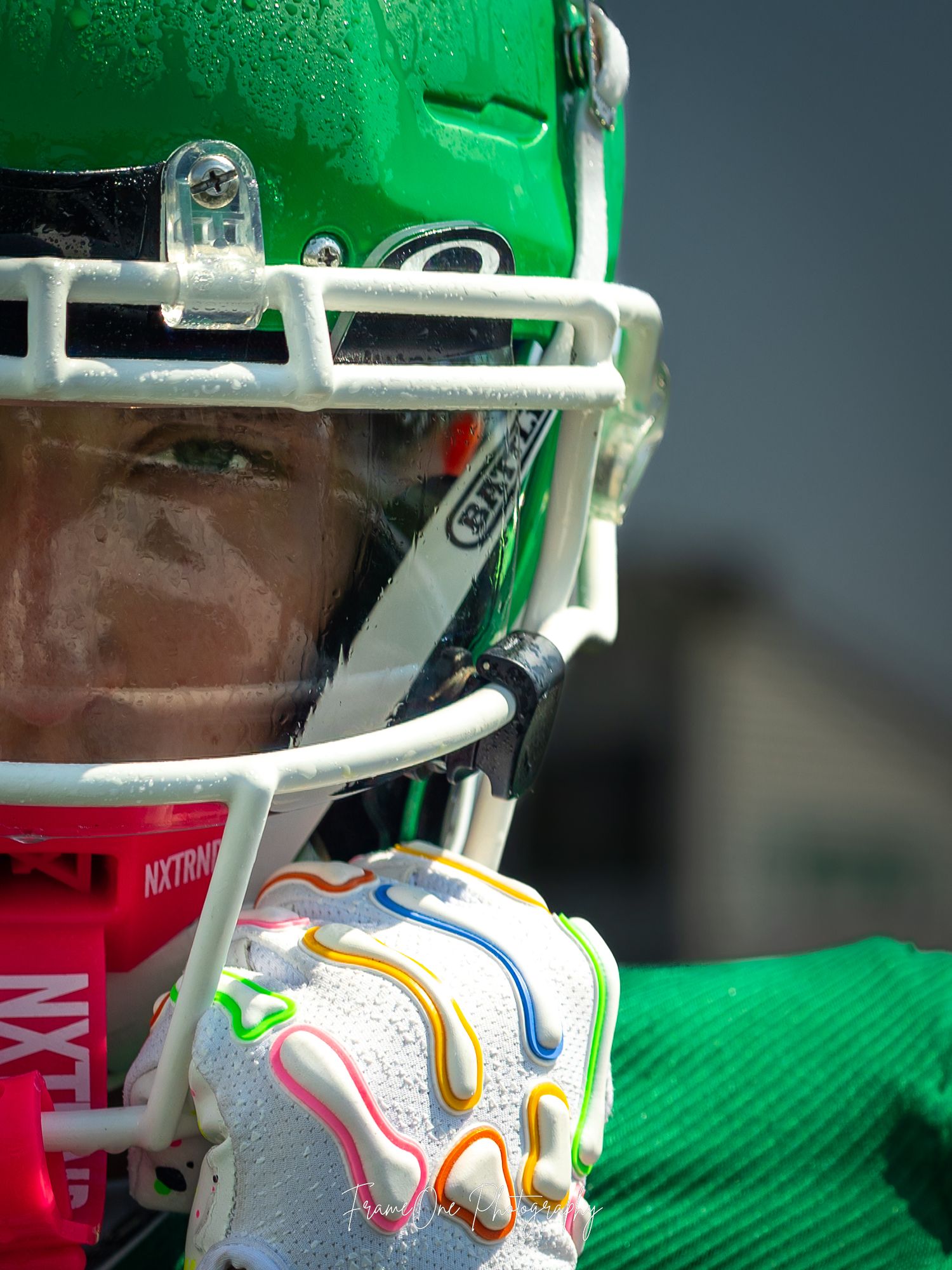 Football facemask details show white and green protective equipment against a dark background with orange and white accents.