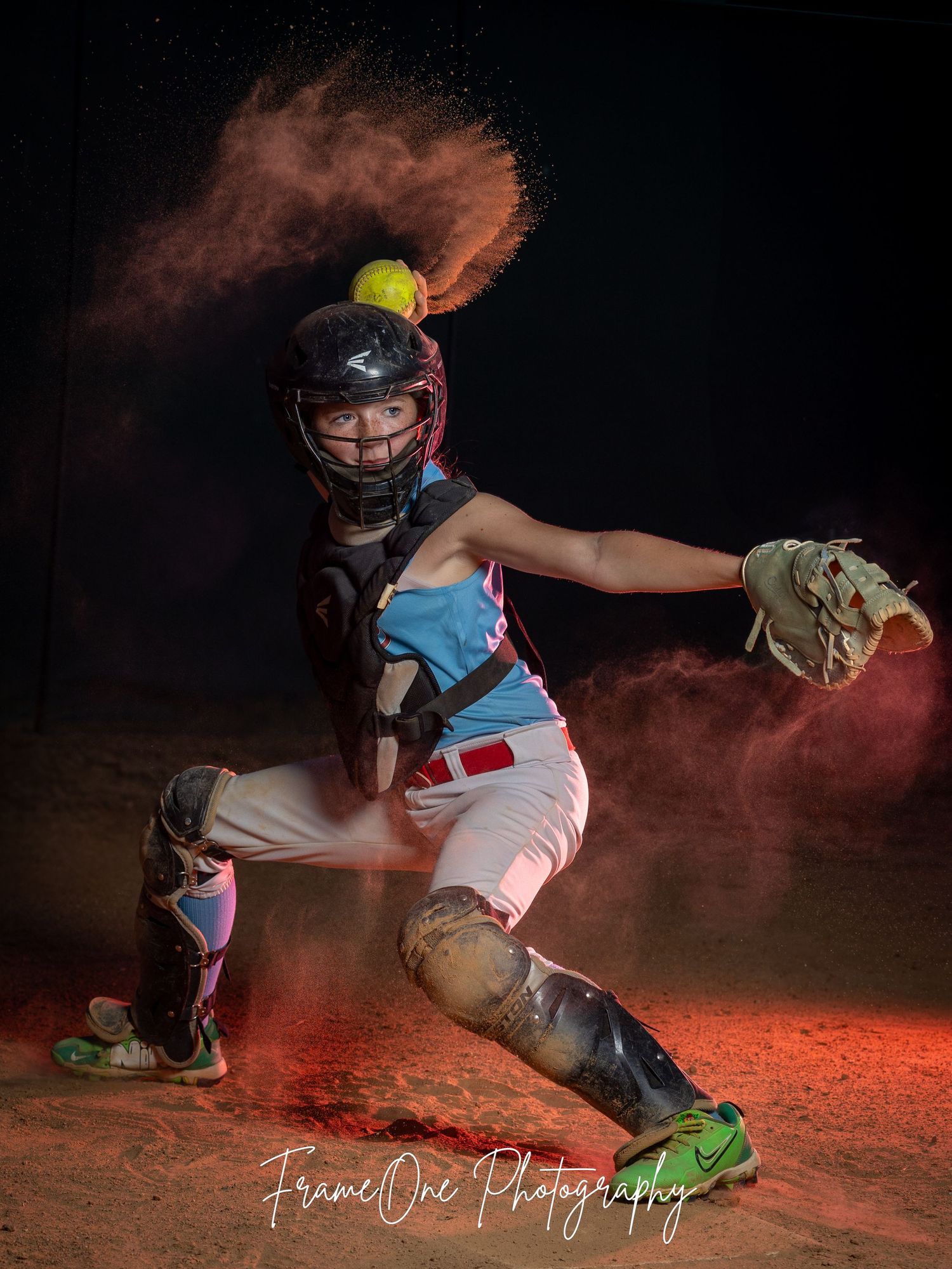 Dramatic sports photo of softball catcher in protective gear with red dust clouds creating dynamic lighting effects.