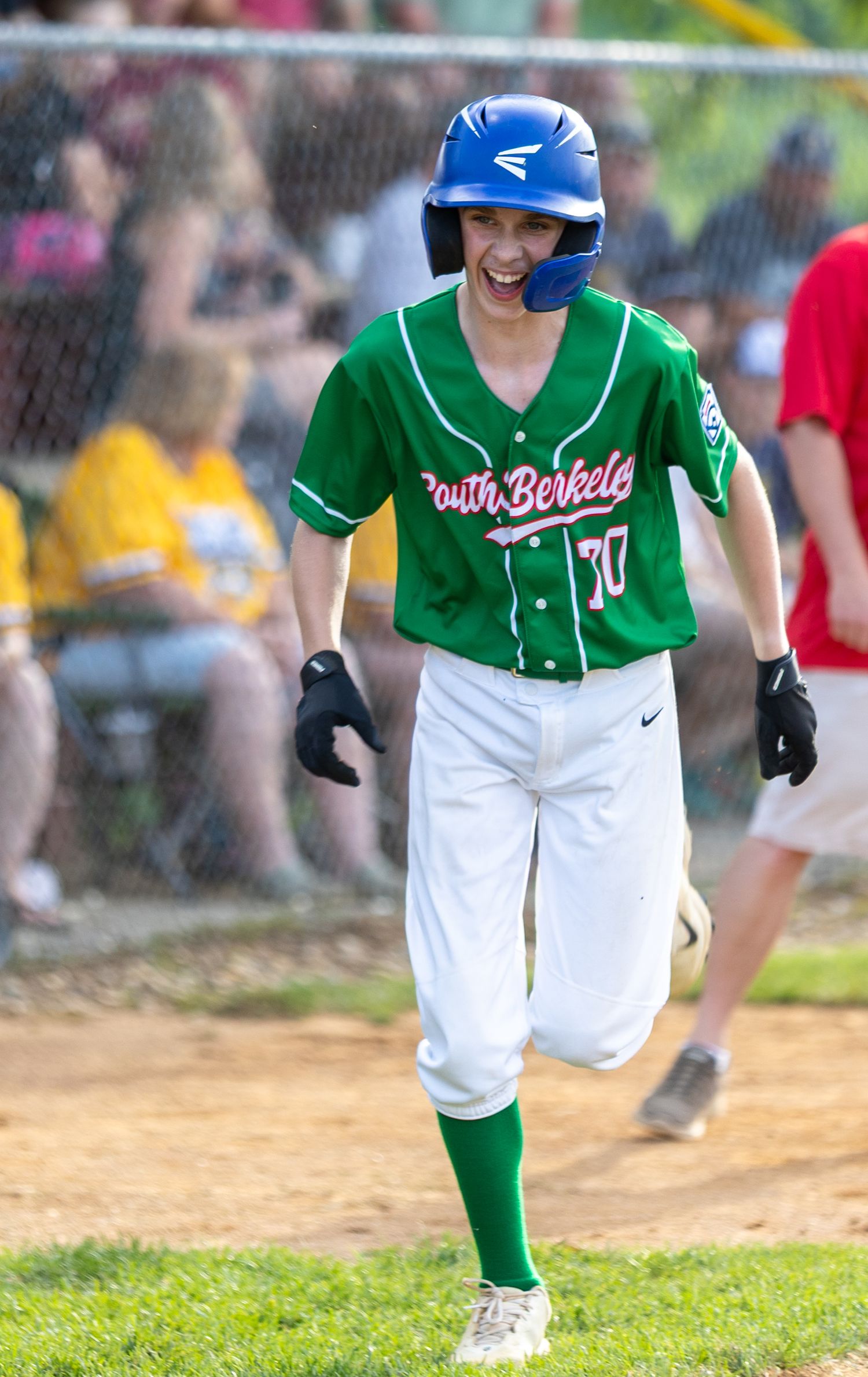 Baseball player in green uniform and blue helmet smiling on baseball field.
