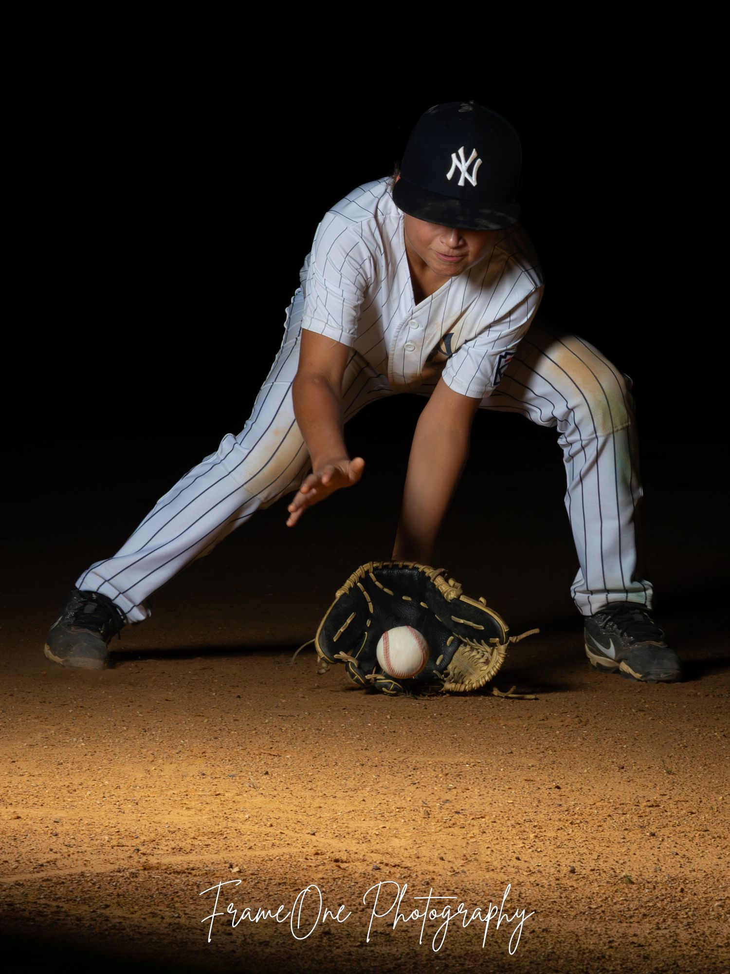 Baseball player in Yankees uniform slides on dirt field reaching for baseball during game action shot.