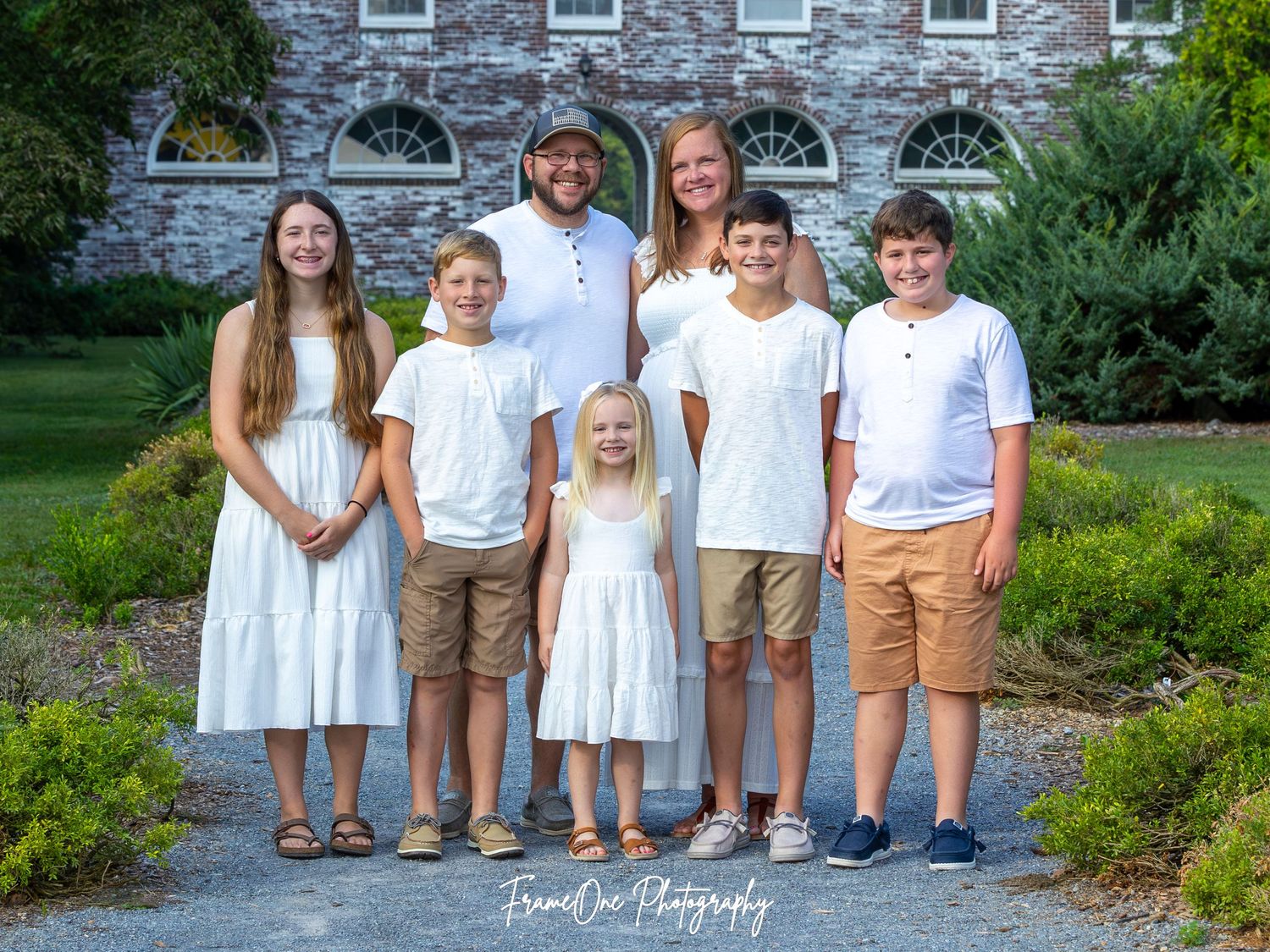 Group of children wearing coordinated white and khaki clothing pose together in an outdoor garden setting.