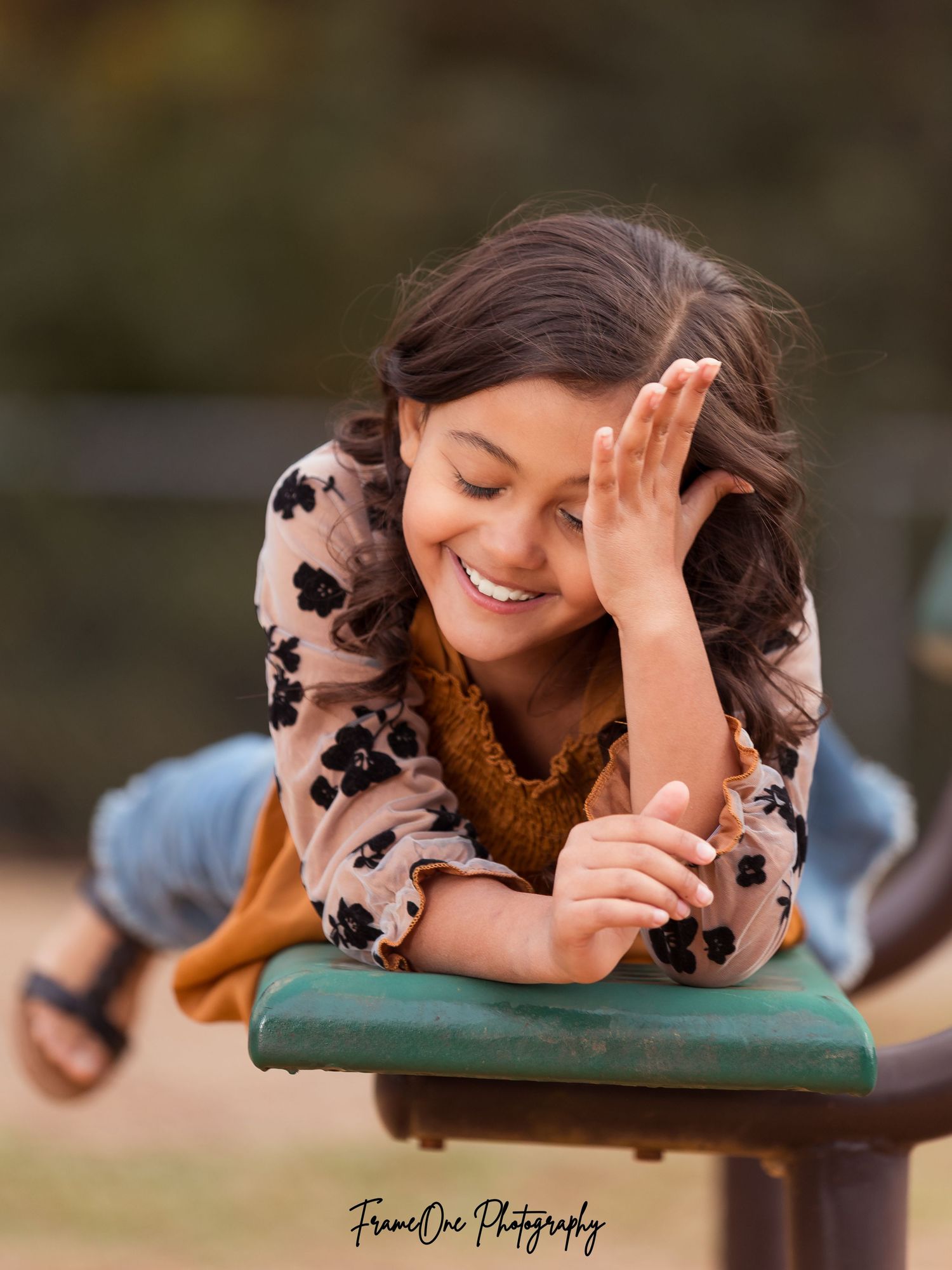 Joyful person in floral print top and brown vest laughs while resting on a green cushioned surface outdoors.