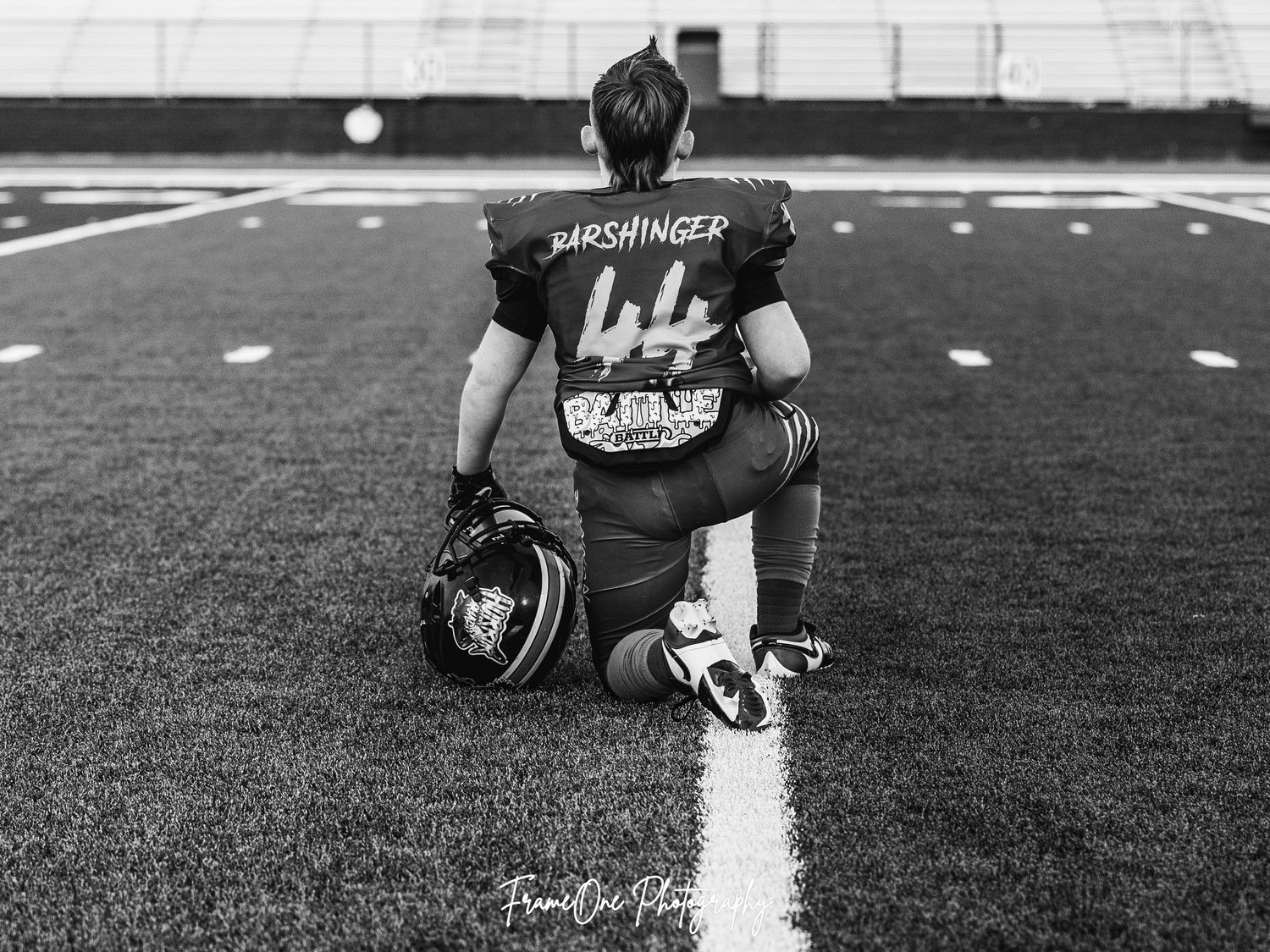 A football player in jersey number 44 kneels thoughtfully on the field in a black and white photograph.