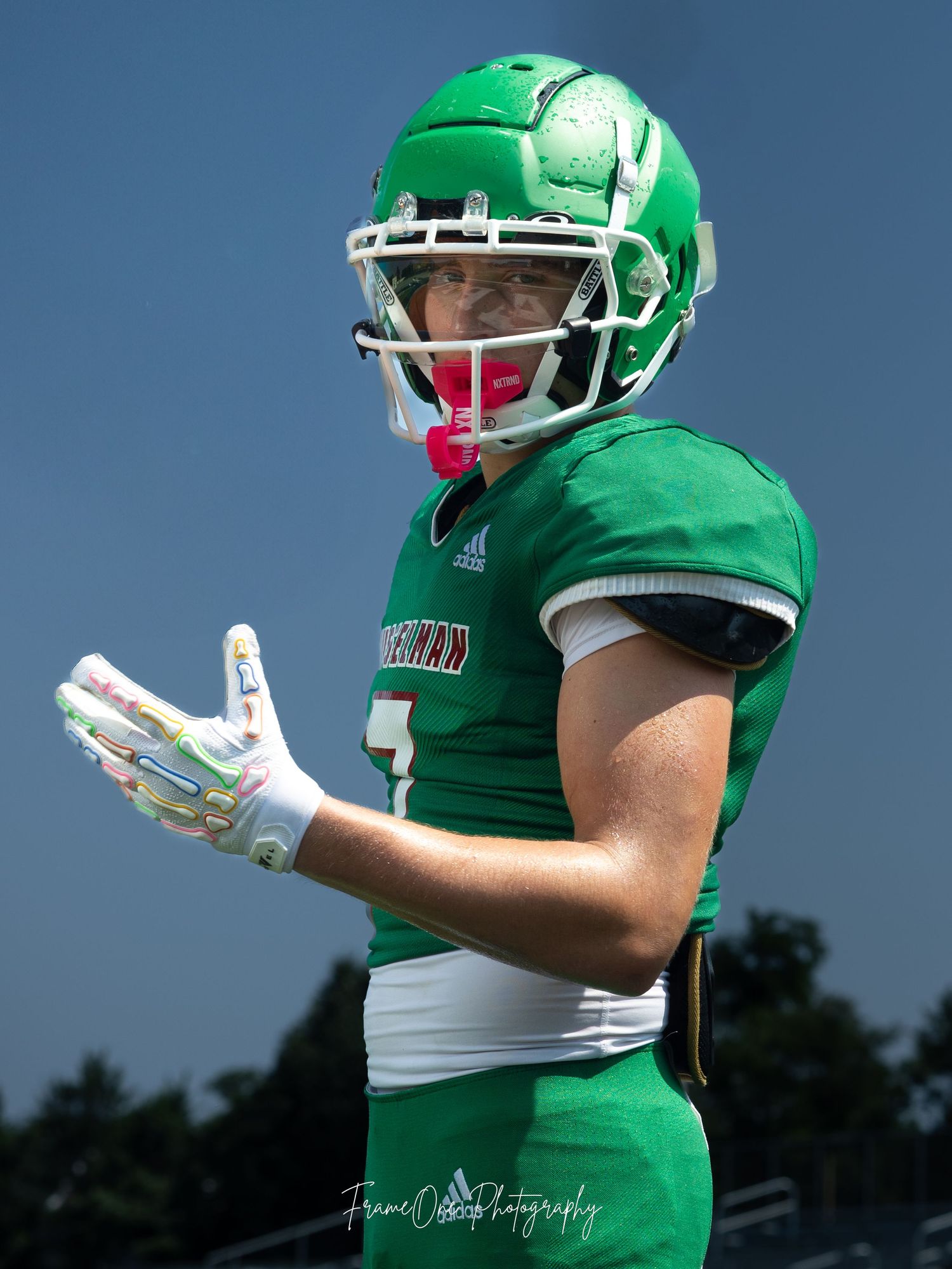 Football player in bright green jersey and white pants poses against blue sky during outdoor practice or game.