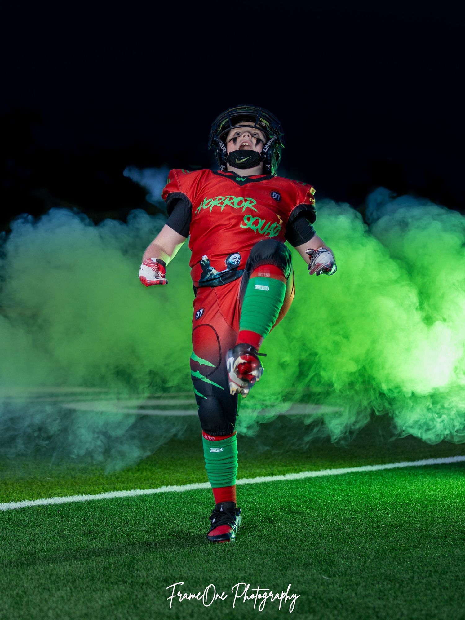 Soccer player strikes dramatic pose in red jersey against vibrant green smoke effect on field at night.
