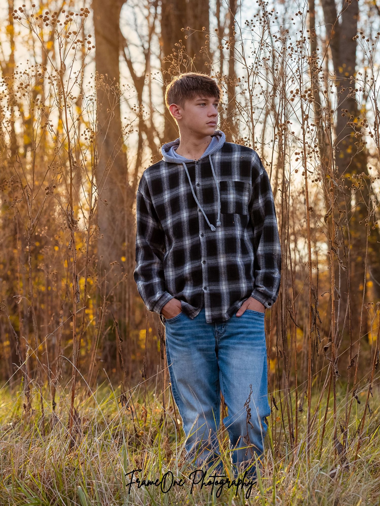 A person wearing a plaid flannel shirt and jeans stands in a sunlit autumn forest during golden hour.