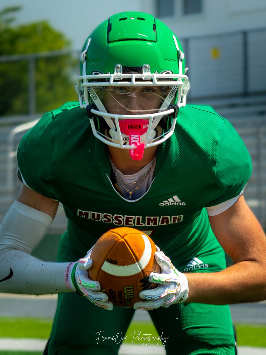 Football player in bright green Marshall University uniform holds ball while wearing protective gear and face mask during game.